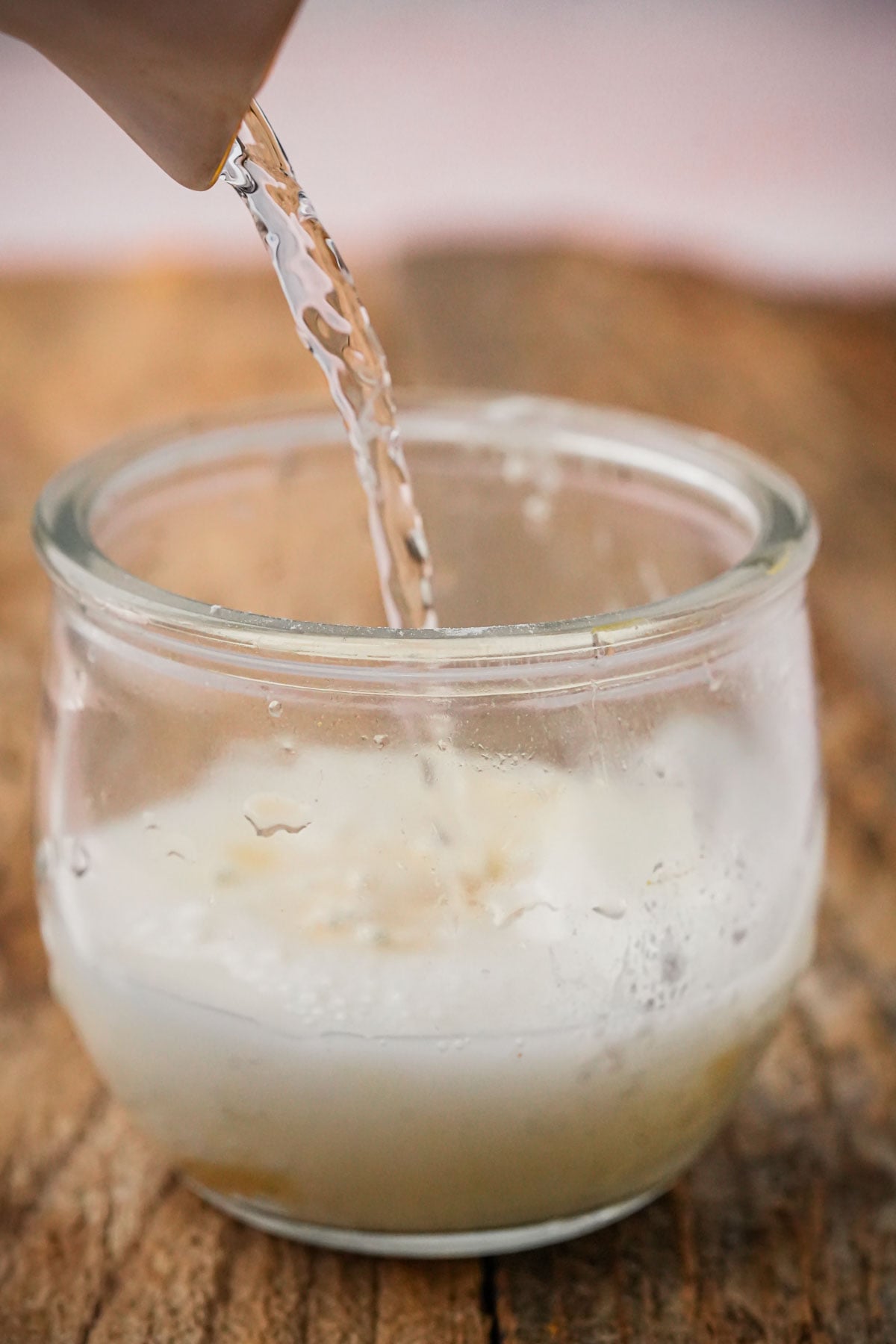 A close-up of liquid being poured from a white container into a glass jar containing starch and agar agar to thicken a vegan pumpkin creme brulee.
