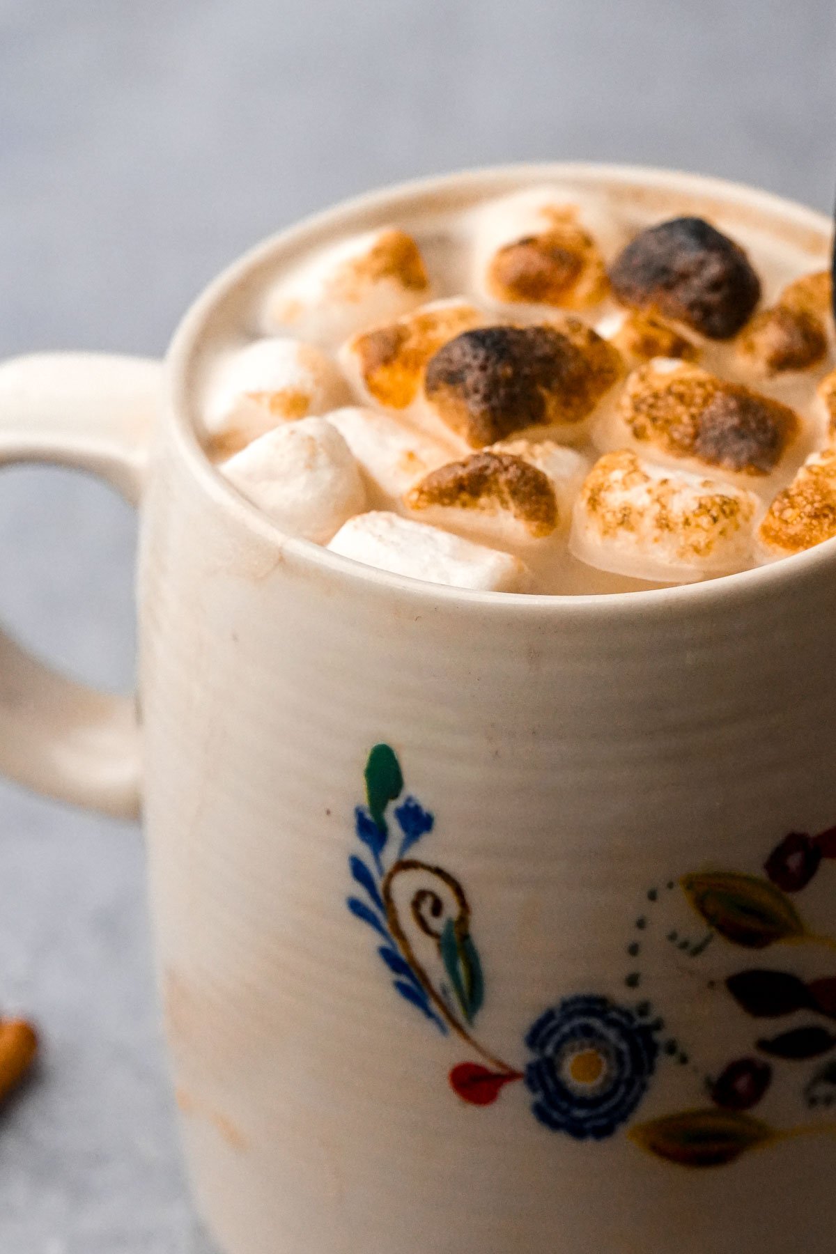 A cream-colored mug with a floral design, filled with vegan gingerbread latte topped with toasted marshmallows.