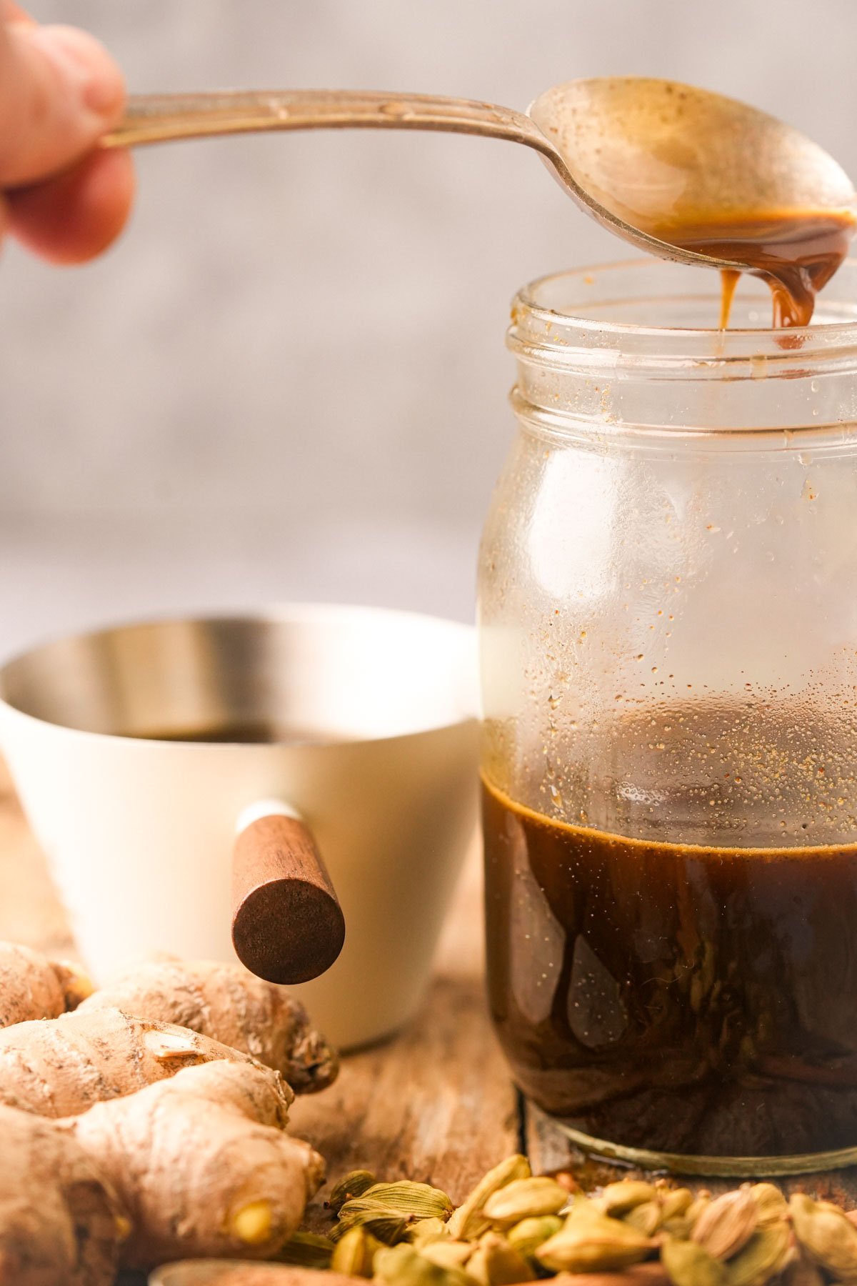 A spoon drizzles gingerbread simple syrup into a glass jar.