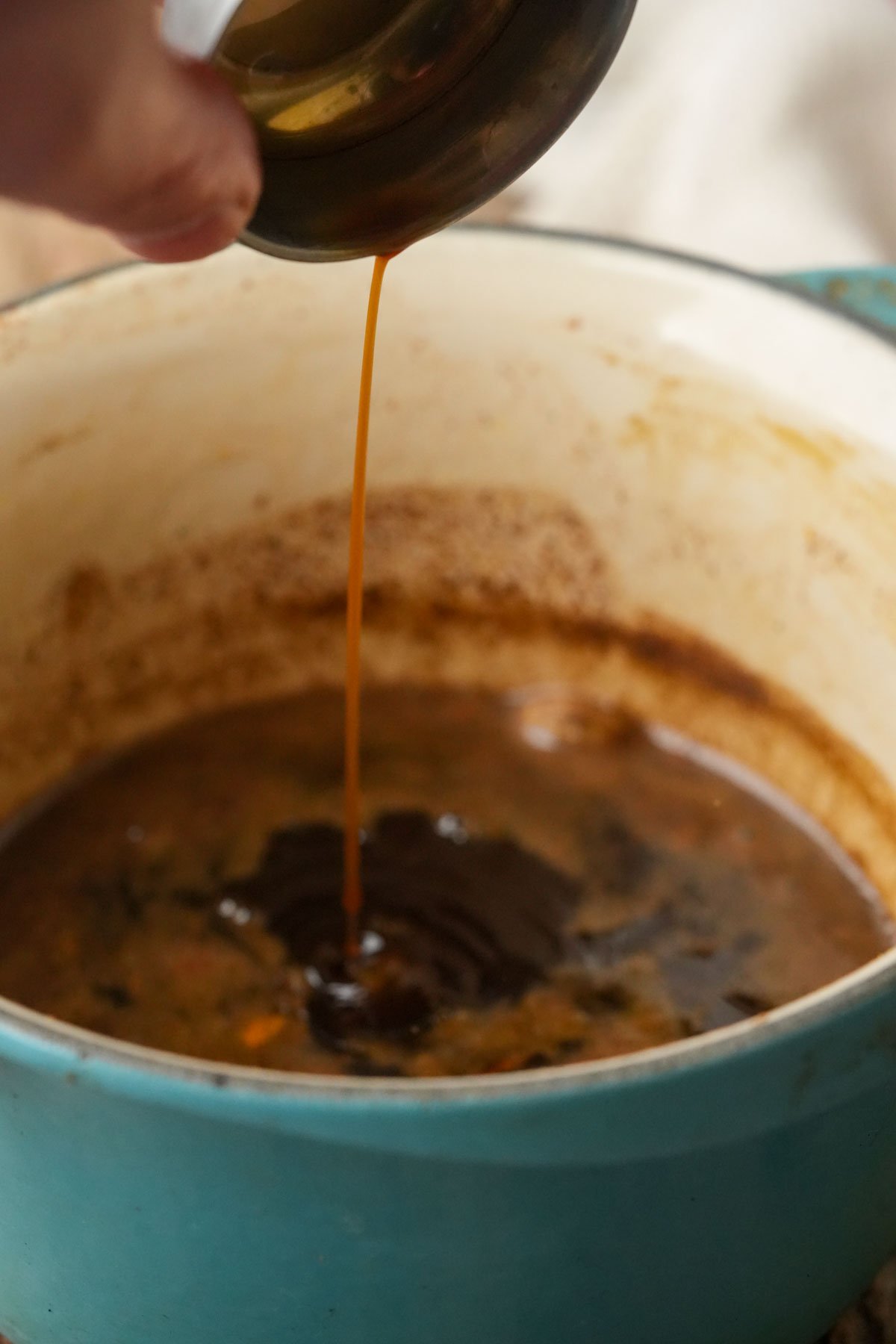 A hand pours a stream of vanilla from a small container into a turquoise pot filled with gingerbread simple syrup.