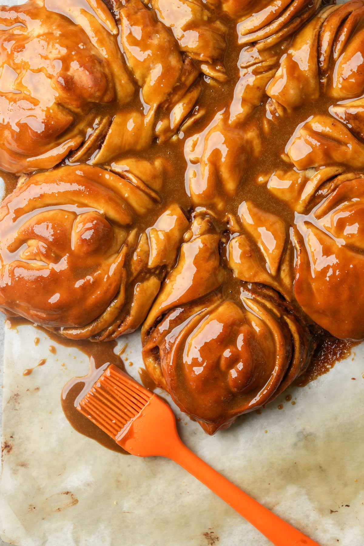 Sticky, golden-brown gingerbread star bread covered in glaze on parchment paper, with an orange silicone pastry brush lying nearby.