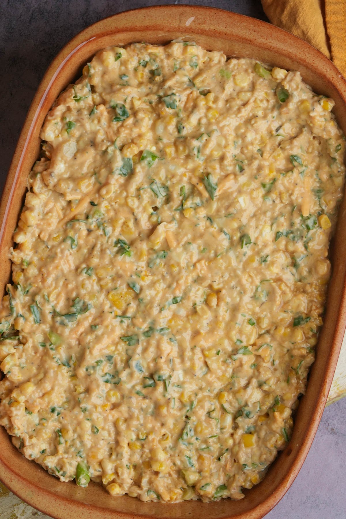 Unbaked vegan corn casserole batter evenly spread in a rectangular, brown ceramic dish.