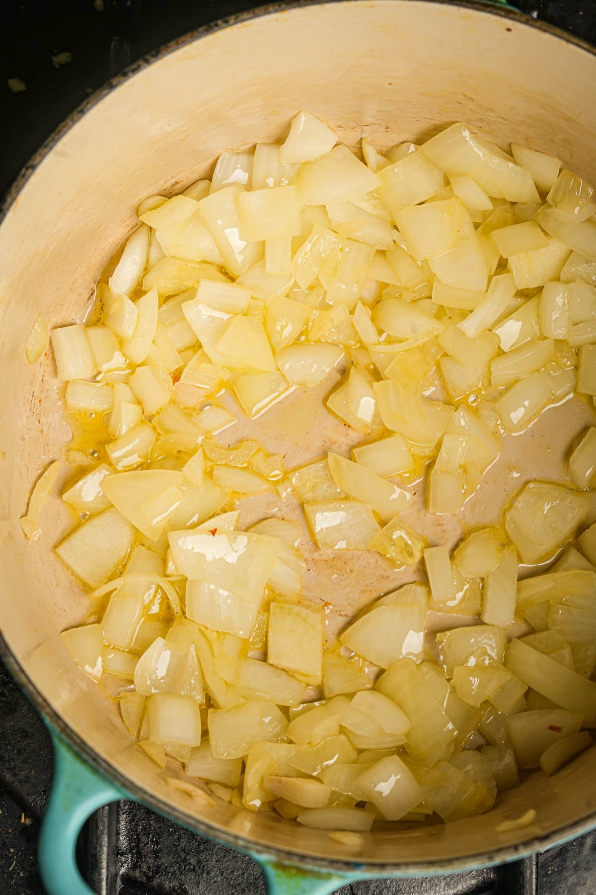 Chopped onions cooking and softening in oil in a large, light-colored pot on a stovetop.