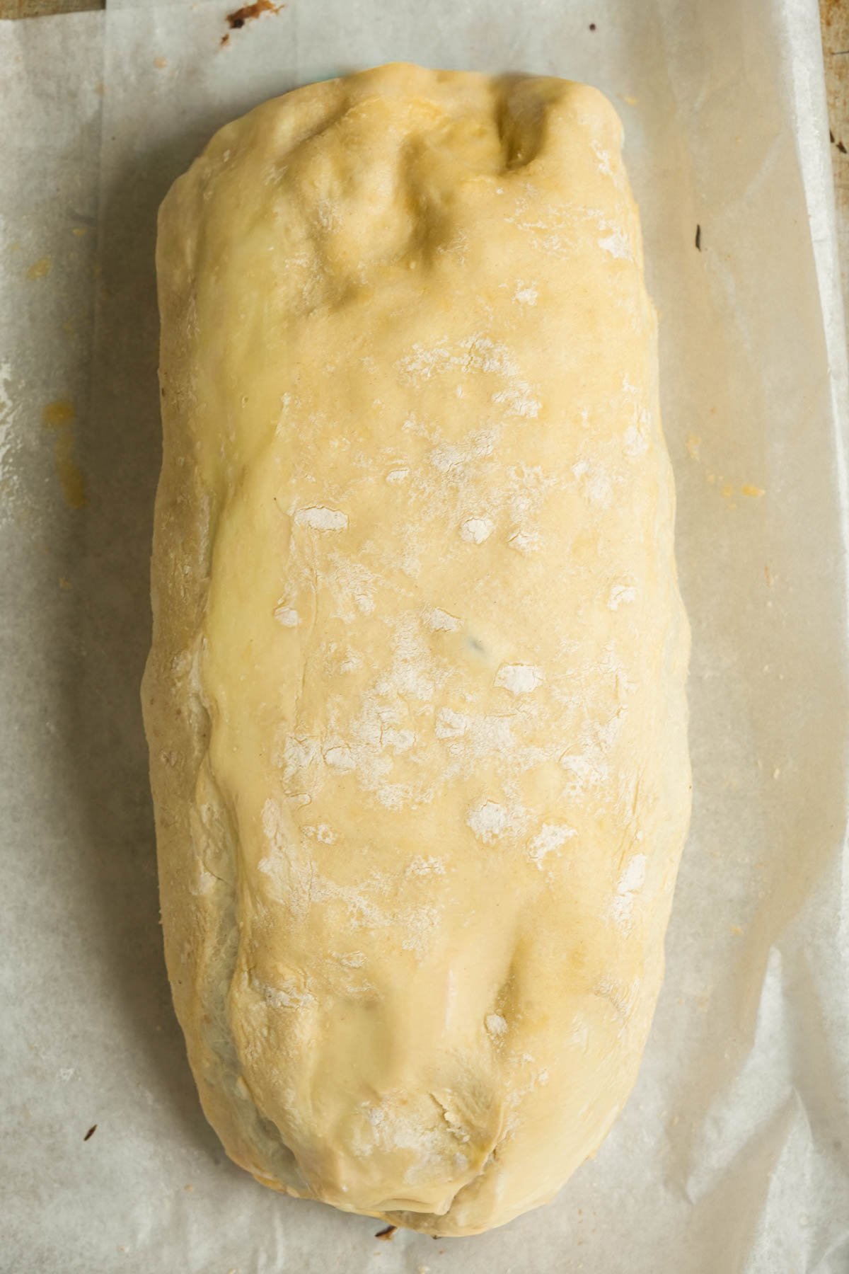 A large, unbaked loaf vegan mushroom Wellington covered in flour sits on parchment paper, ready for baking.