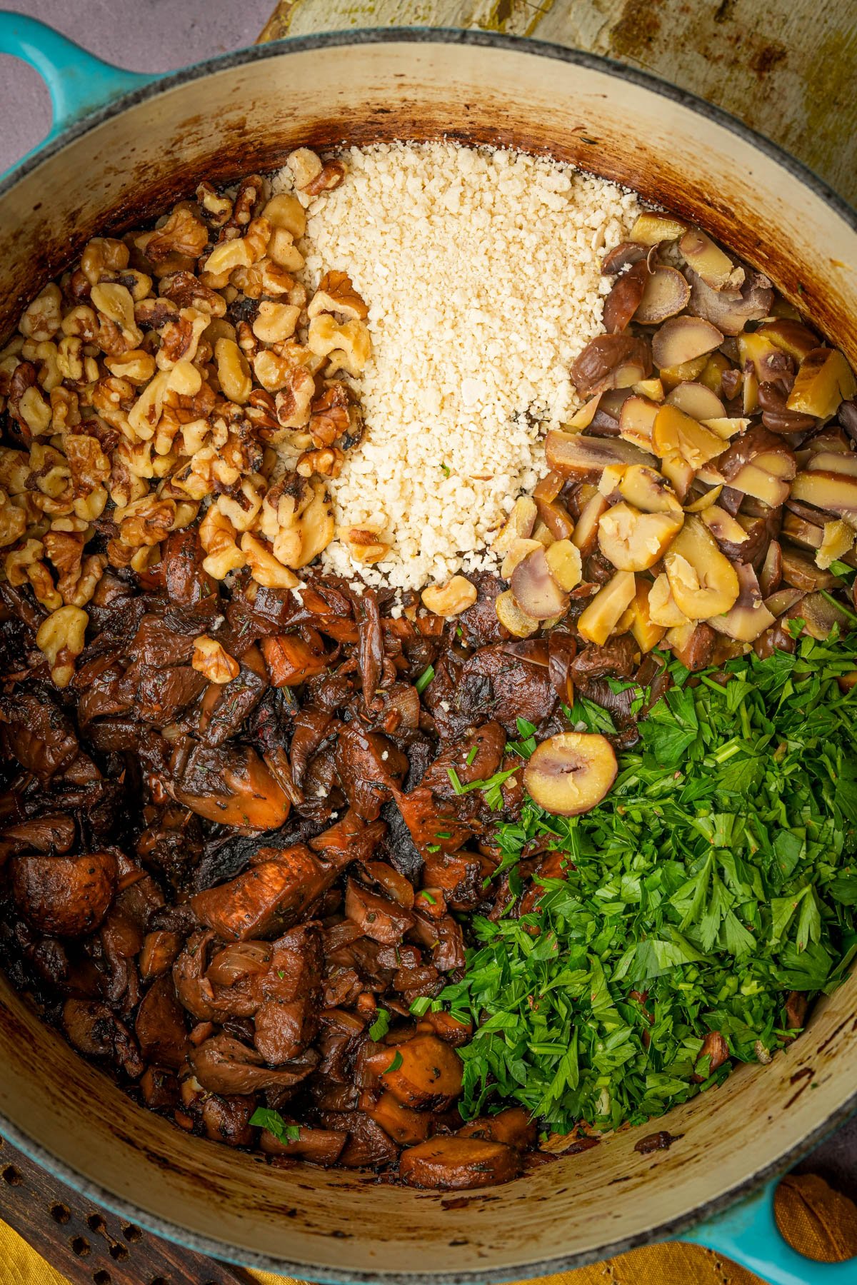 A pot filled with chopped walnuts, panko, chopped mushrooms, cooked brown mushrooms, fresh parsley, and diced chestnuts arranged in sections before mixing to become vegan mushroom Wellington filling.