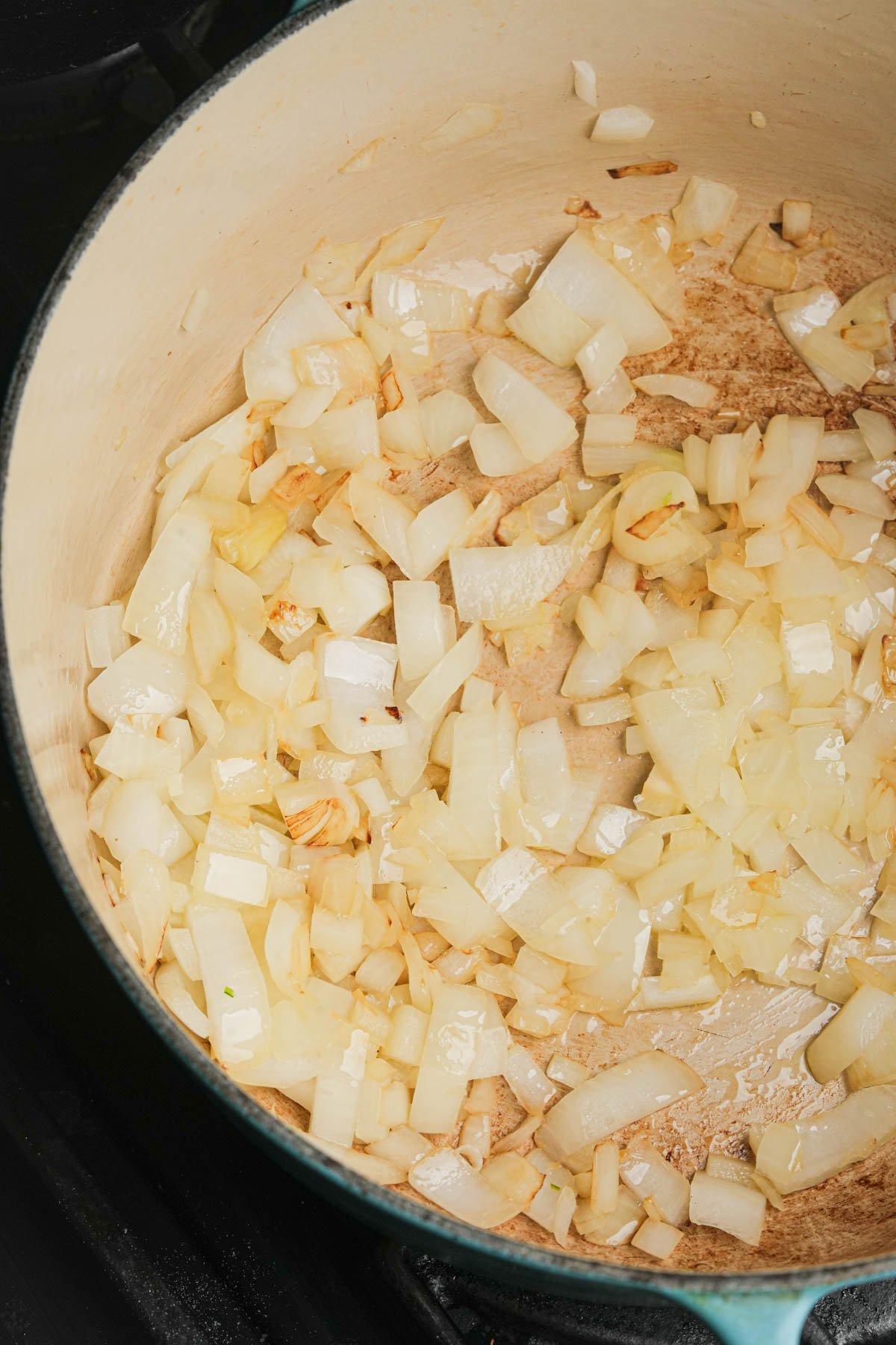 Chopped onions are being sautéed in a light-colored pot, showing light browning and softening on the vegetables.