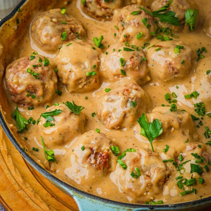 Vegan Swedish meatballs coated in creamy brown gravy, garnished with chopped parsley and chives, in a skillet on a wooden surface.
