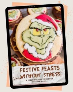 A tablet displays a vegan holiday cookbook cover featuring a decorated cookie with a Grinch face in a Santa hat. The title reads Festive Feasts Without Stress by Adam Sobel.