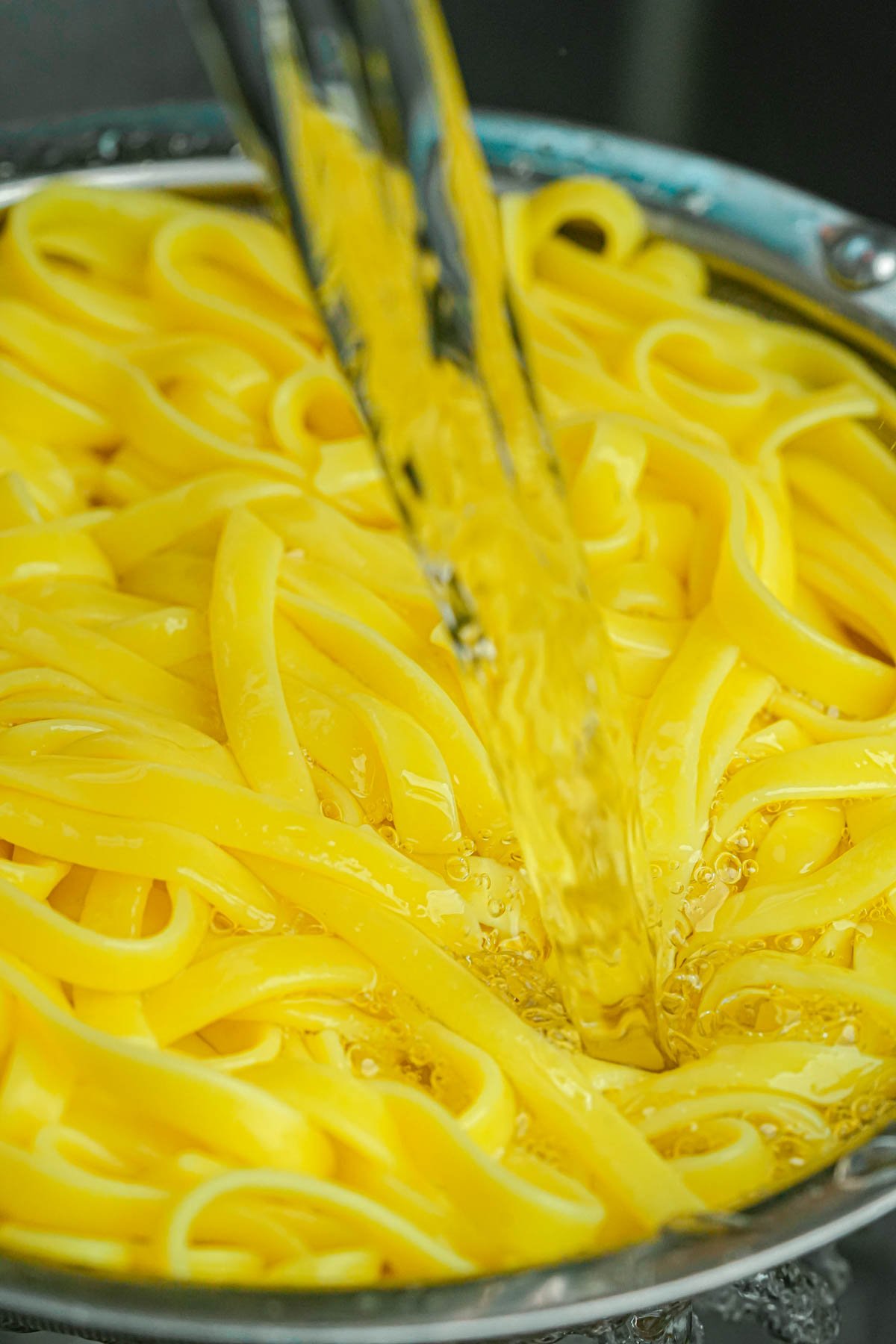 Yellow mi quang noodles are rinsed with a stream of water in a metal colander.