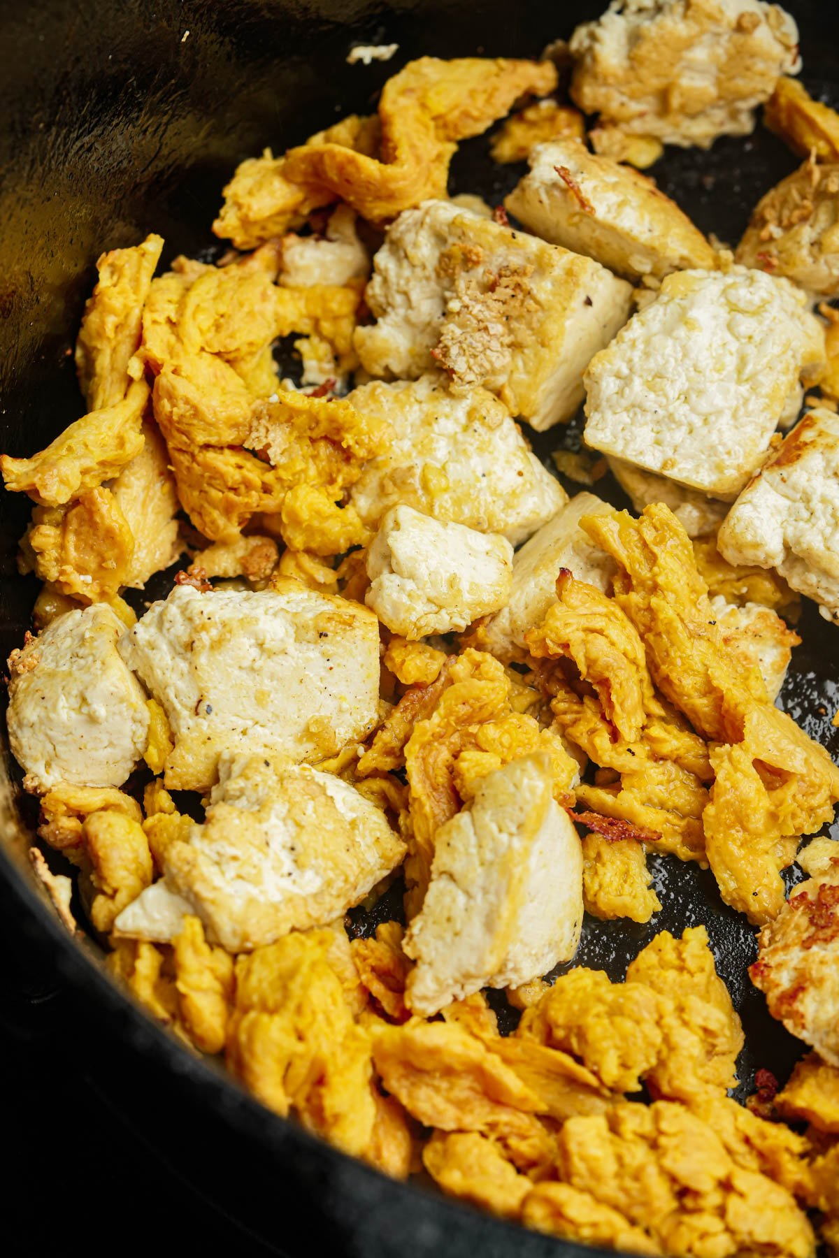 Soy curls and chunks of tofu cooking in a black skillet, with both ingredients lightly browned.