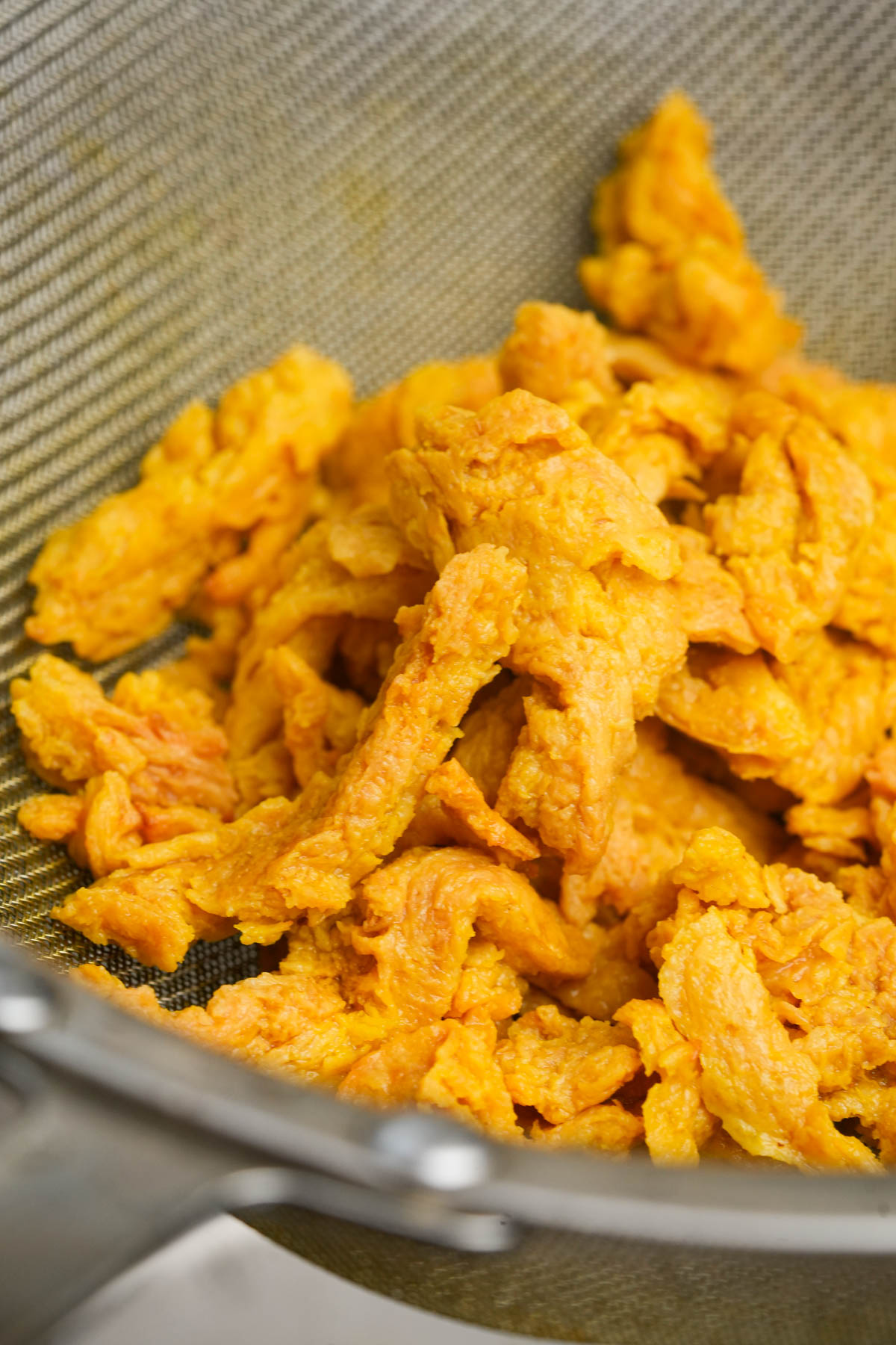 Pieces of rehydrated soy curls draining in a metal strainer.