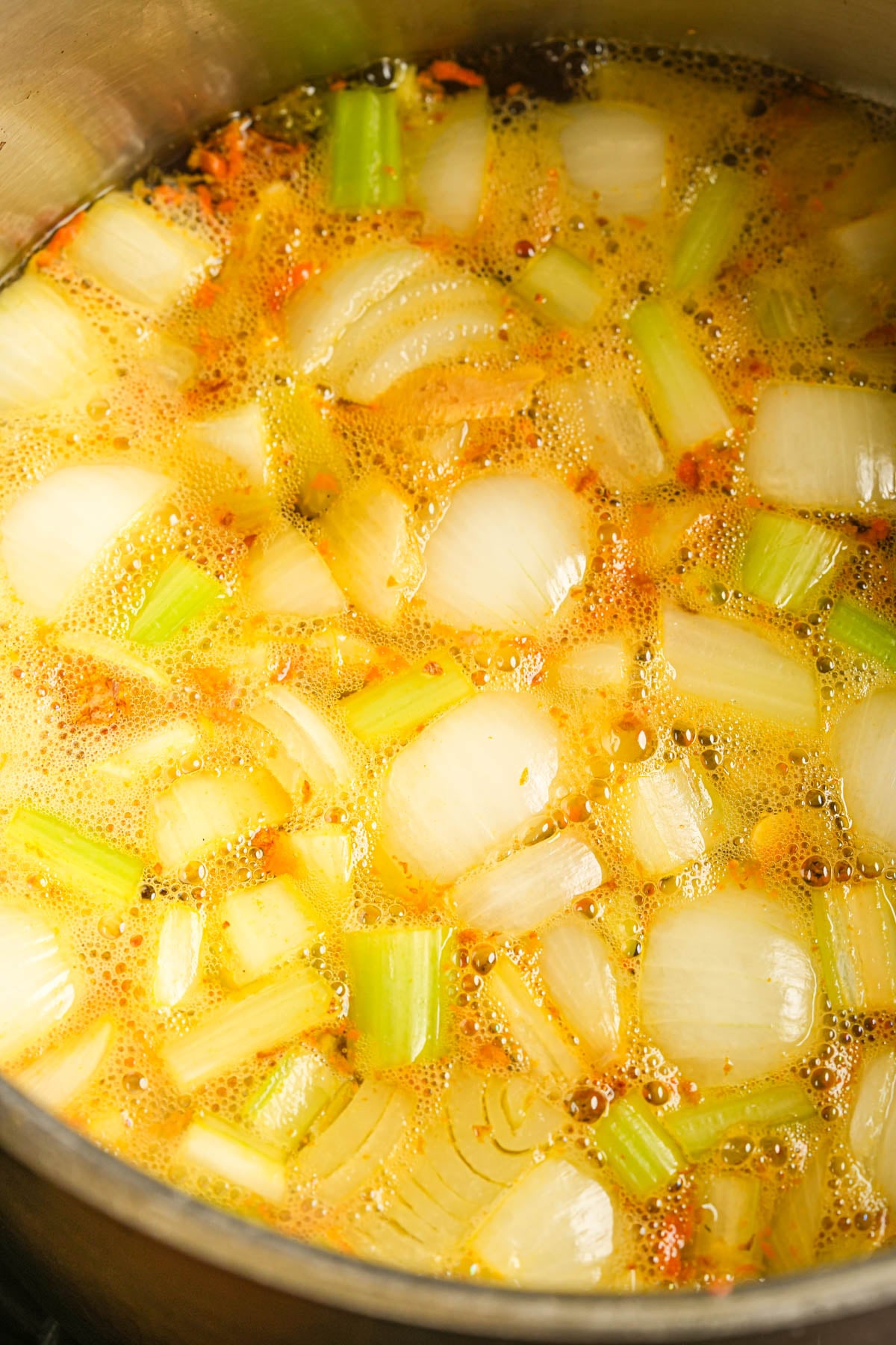 Chopped onions, turmeric, and celery simmer in a pot.