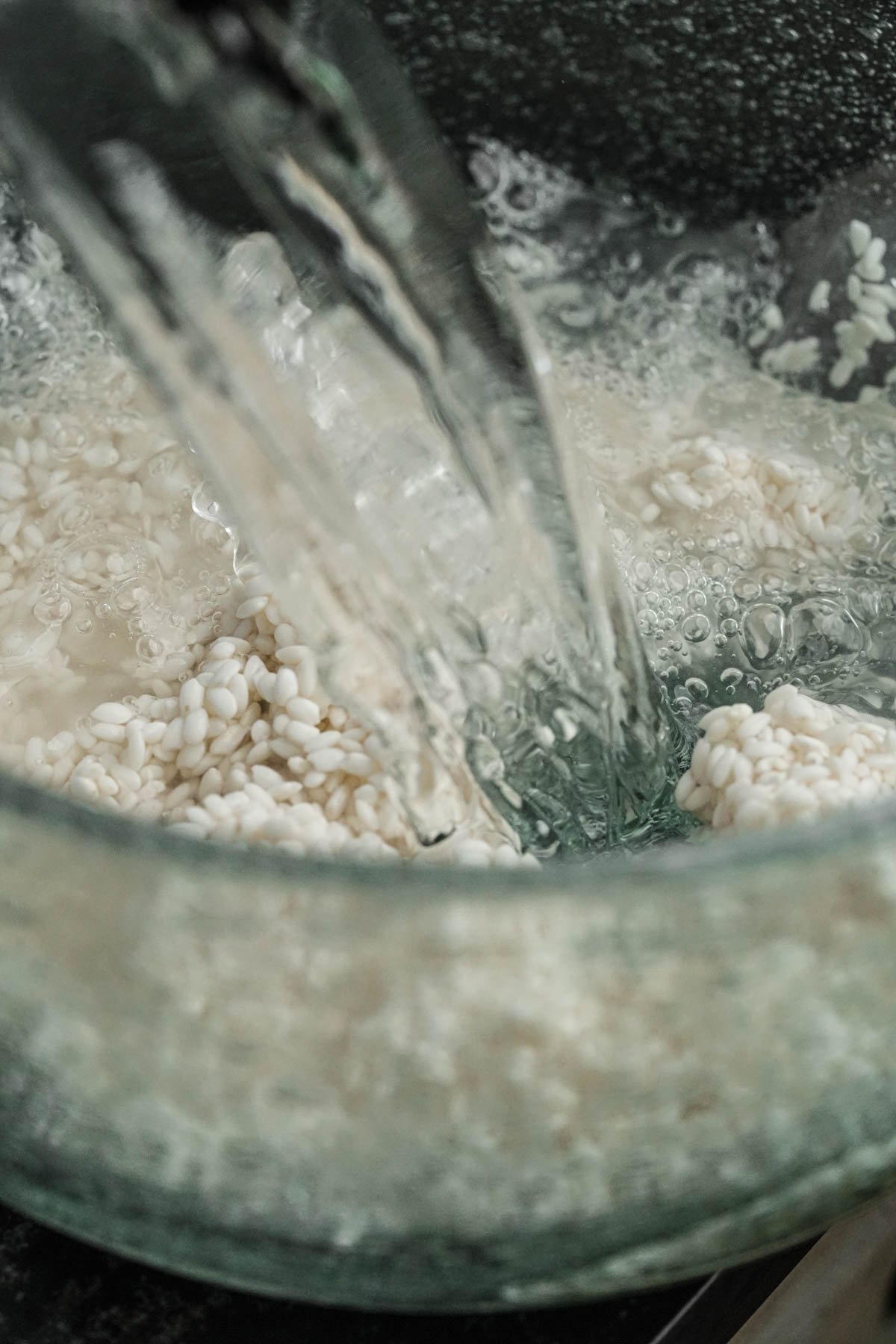 Water being poured into a glass bowl containing uncooked Vietnamese sticky rice.
