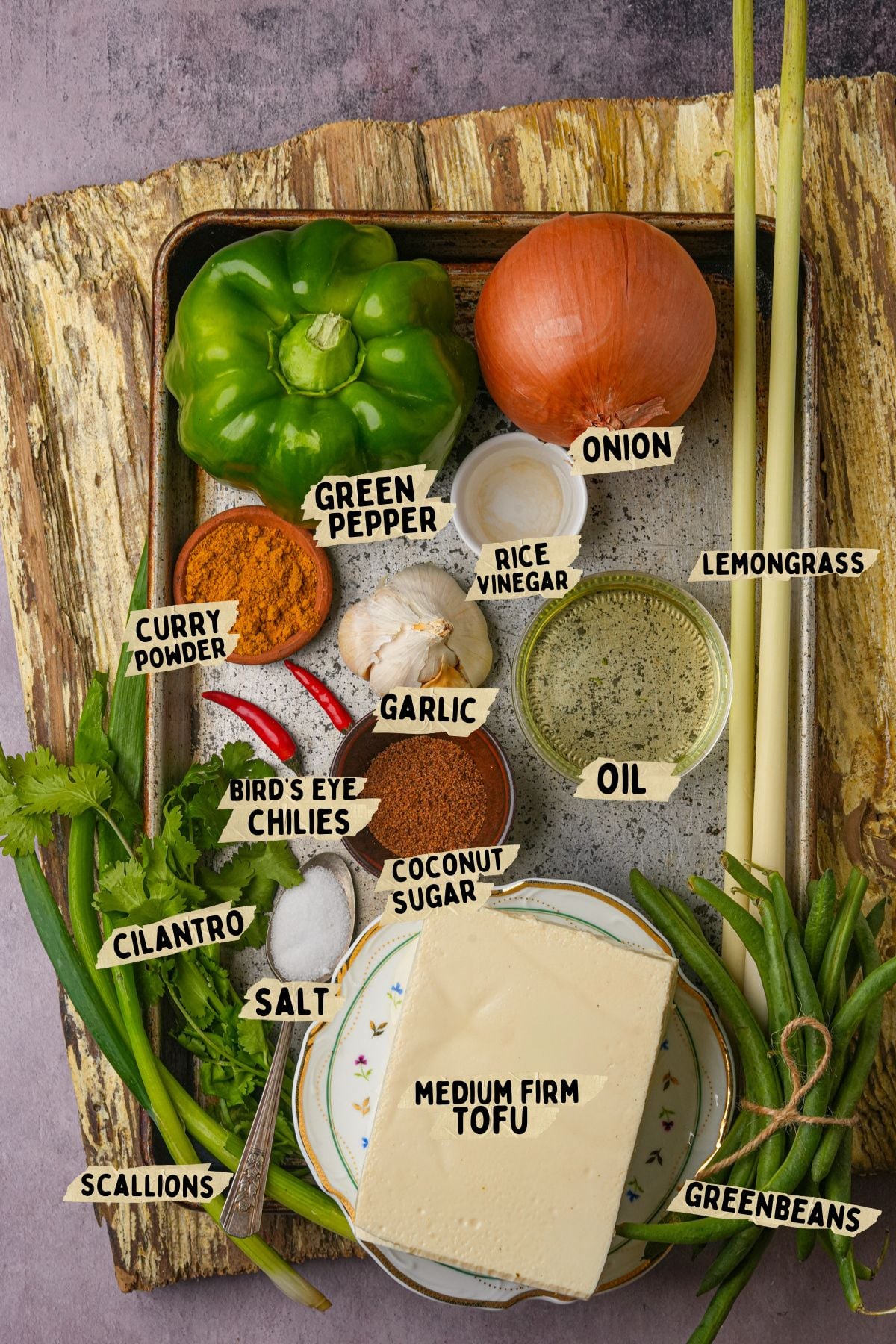 A tray with labeled ingredients for a lemongrass tofu recipe, including green pepper, onion, lemongrass, oil, coconut sugar, rice vinegar, garlic, bird's eye chilies, curry powder, cilantro, salt, scallions, green beans, and medium firm tofu.