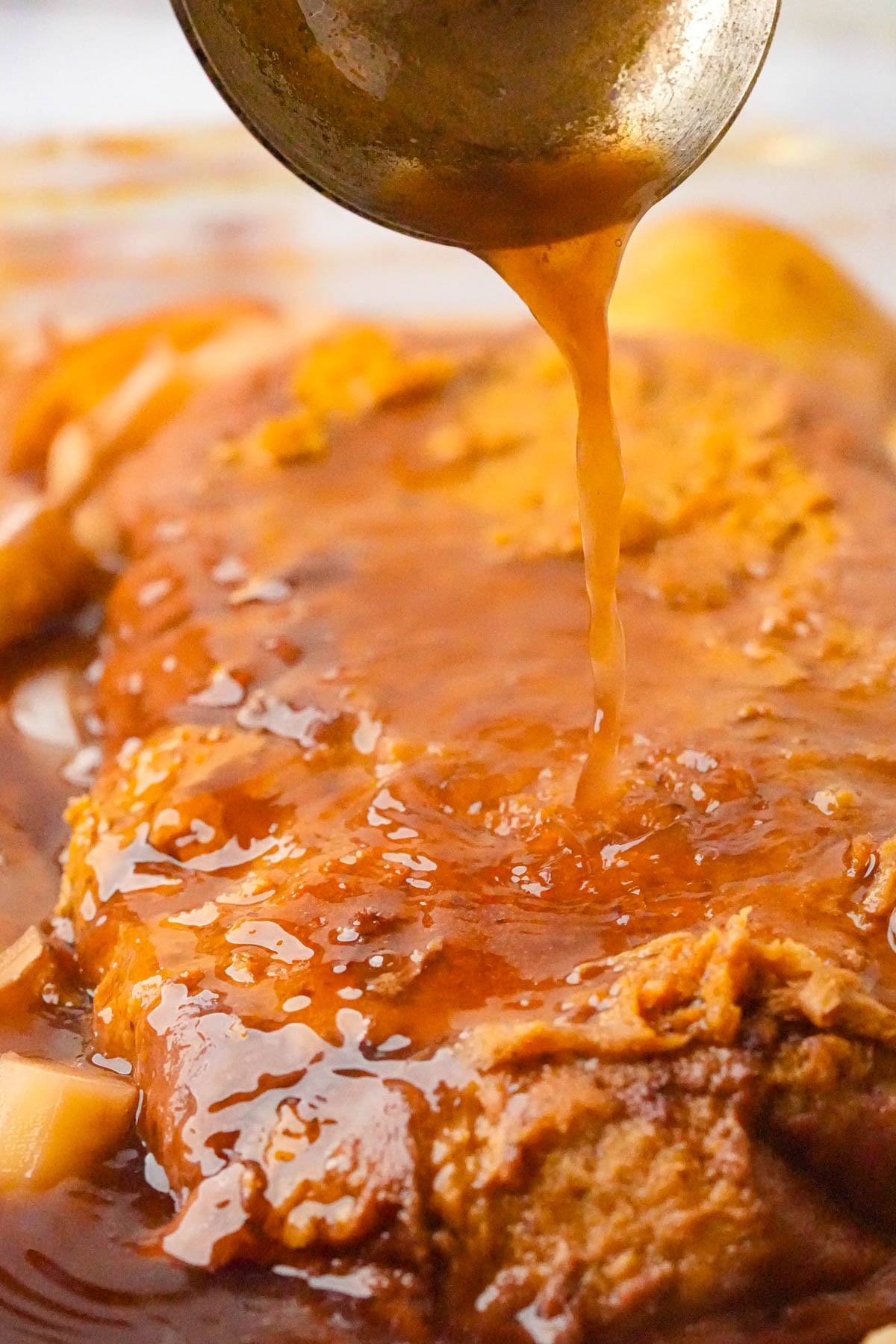 Close-up of a tender piece of Jewish vegan brisket covered in rich wine infused broth with a ladle pouring more liquid over the top.