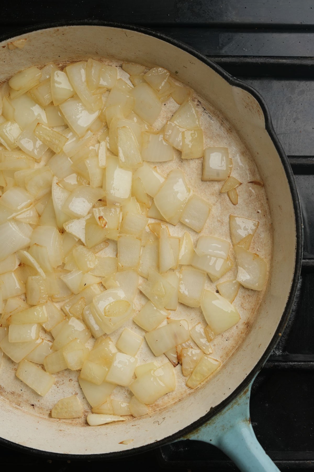 A light blue skillet filled with chopped onions sautéing on a stovetop; the onions are turning translucent, indicating they are being cooked.