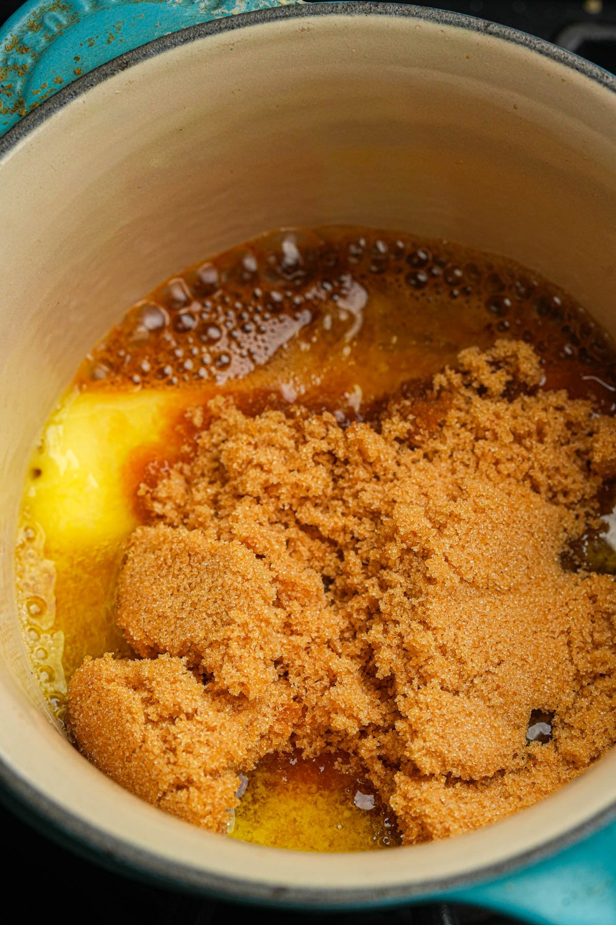 A close-up of a pot with melting butter and a heap of brown sugar, beginning to caramelize together.