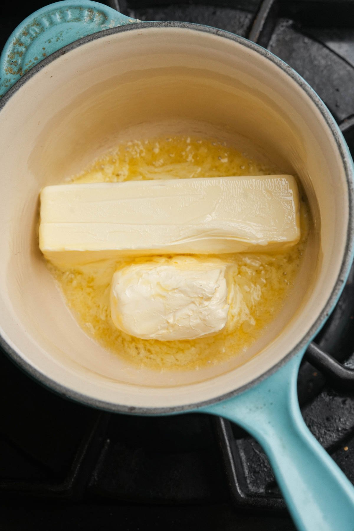 A blue pot on a stove contains a melting stick of vegan butter.