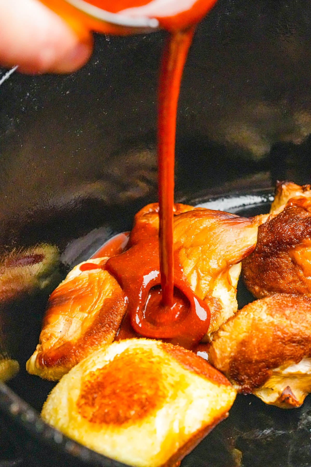 Marinade being poured over browned pieces of lion's mane in a black cooking pot.