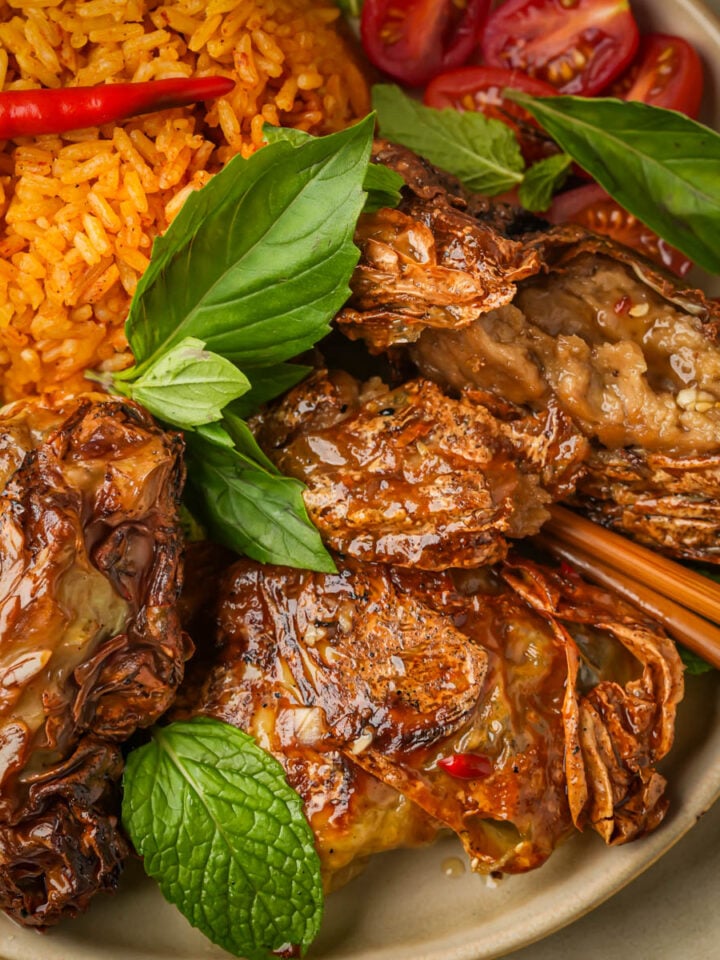 A plate of vegan Vietnamese fried chicken with herbs, red rice, fresh lime, cherry tomatoes, and garnished with basil and mint leaves, with chopsticks resting on the side.