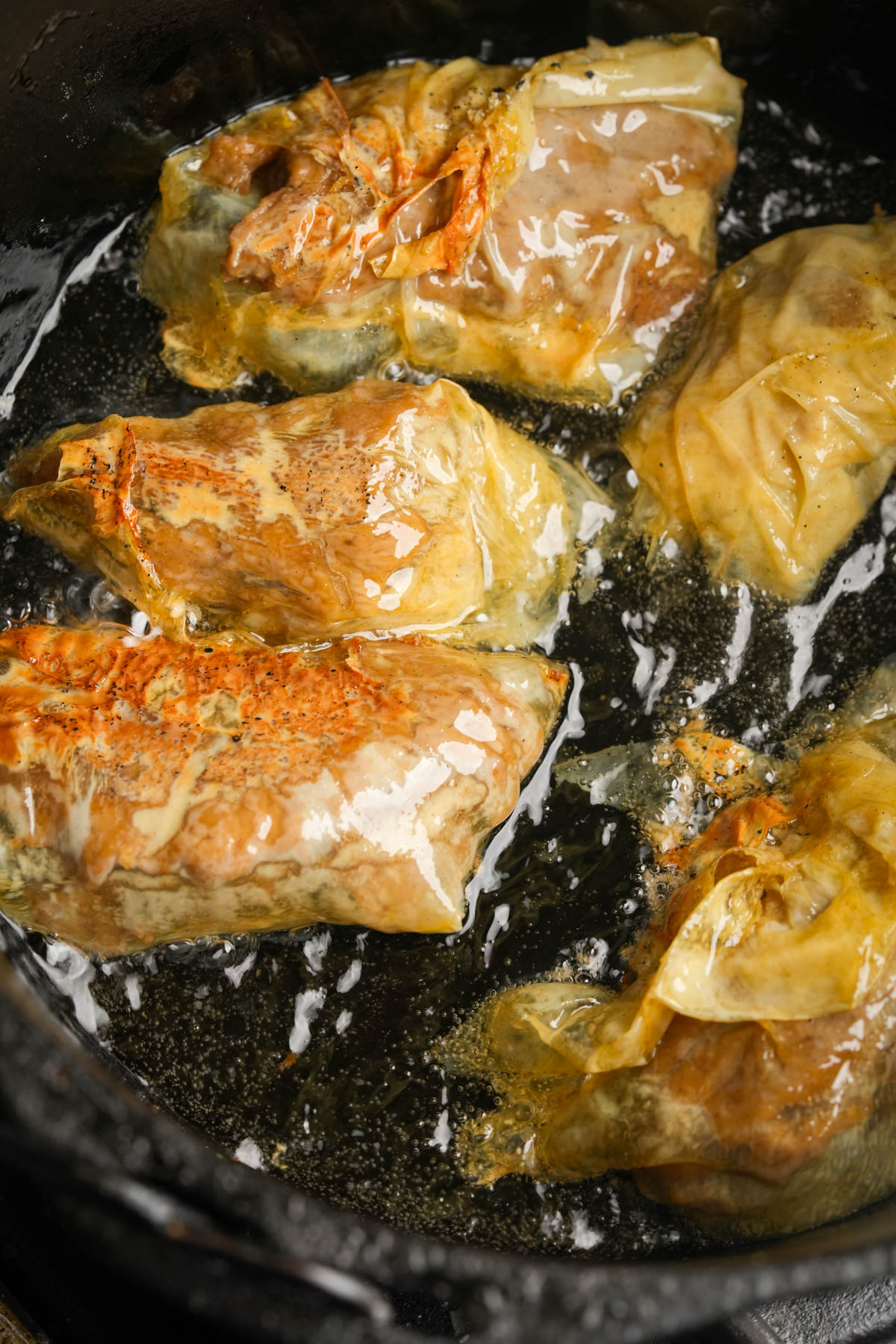 Four vegan Vietnamese fried chicken pieces are cooking in a pan with oil.