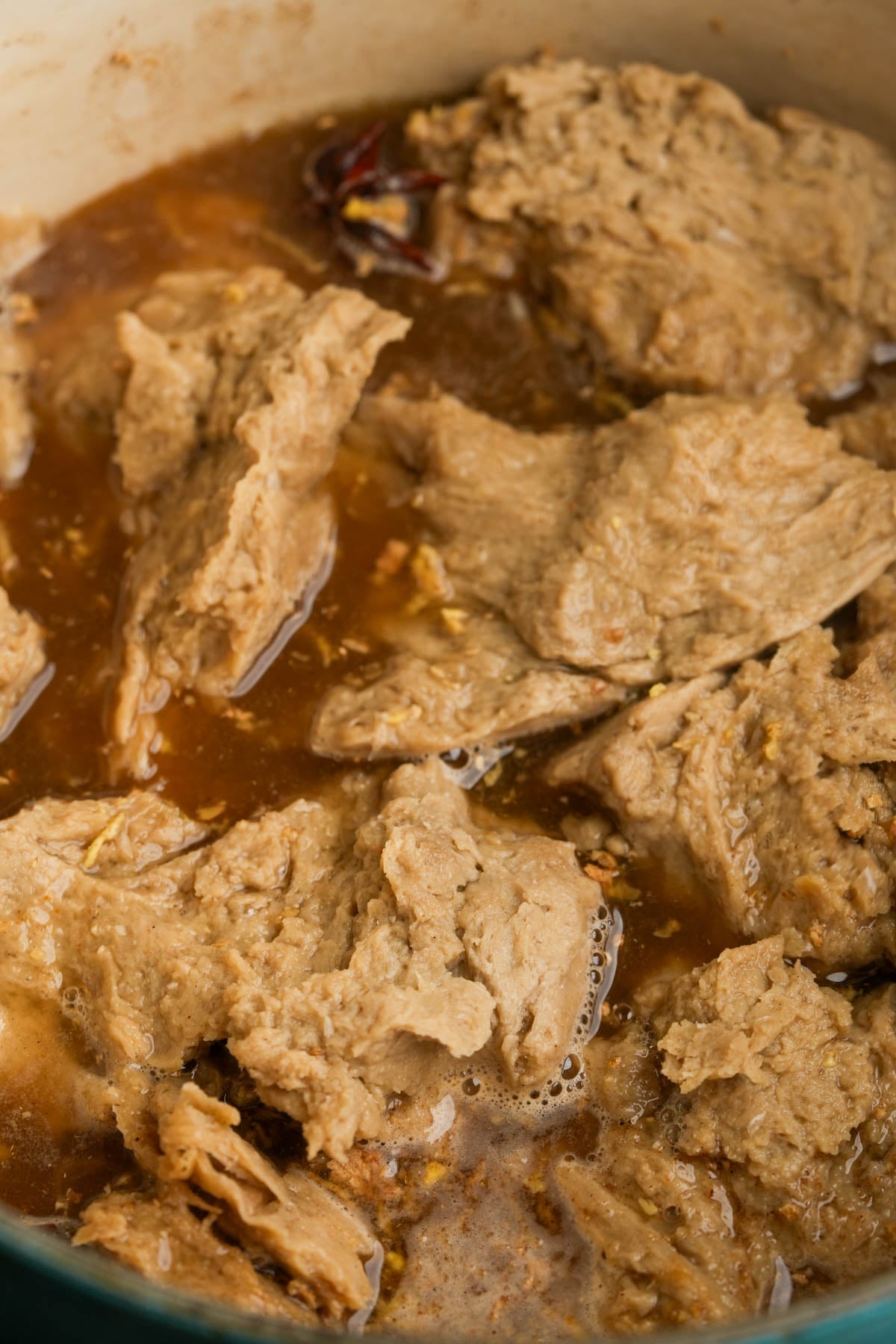 Chunks of seitan simmer in a brown broth with visible spices and a few pieces of star anise.