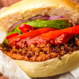 A vegan torta de chorizo filled with red peppers, avocado slices, onions, and sauce, all in a toasted bun.