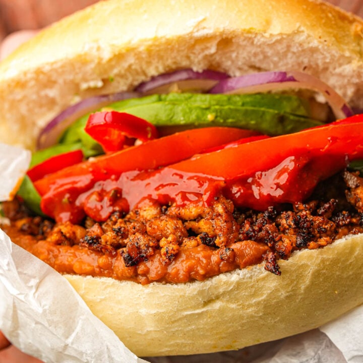 A vegan torta de chorizo filled with red peppers, avocado slices, onions, and sauce, all in a toasted bun.