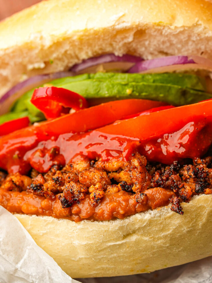A vegan torta de chorizo filled with red peppers, avocado slices, onions, and sauce, all in a toasted bun.