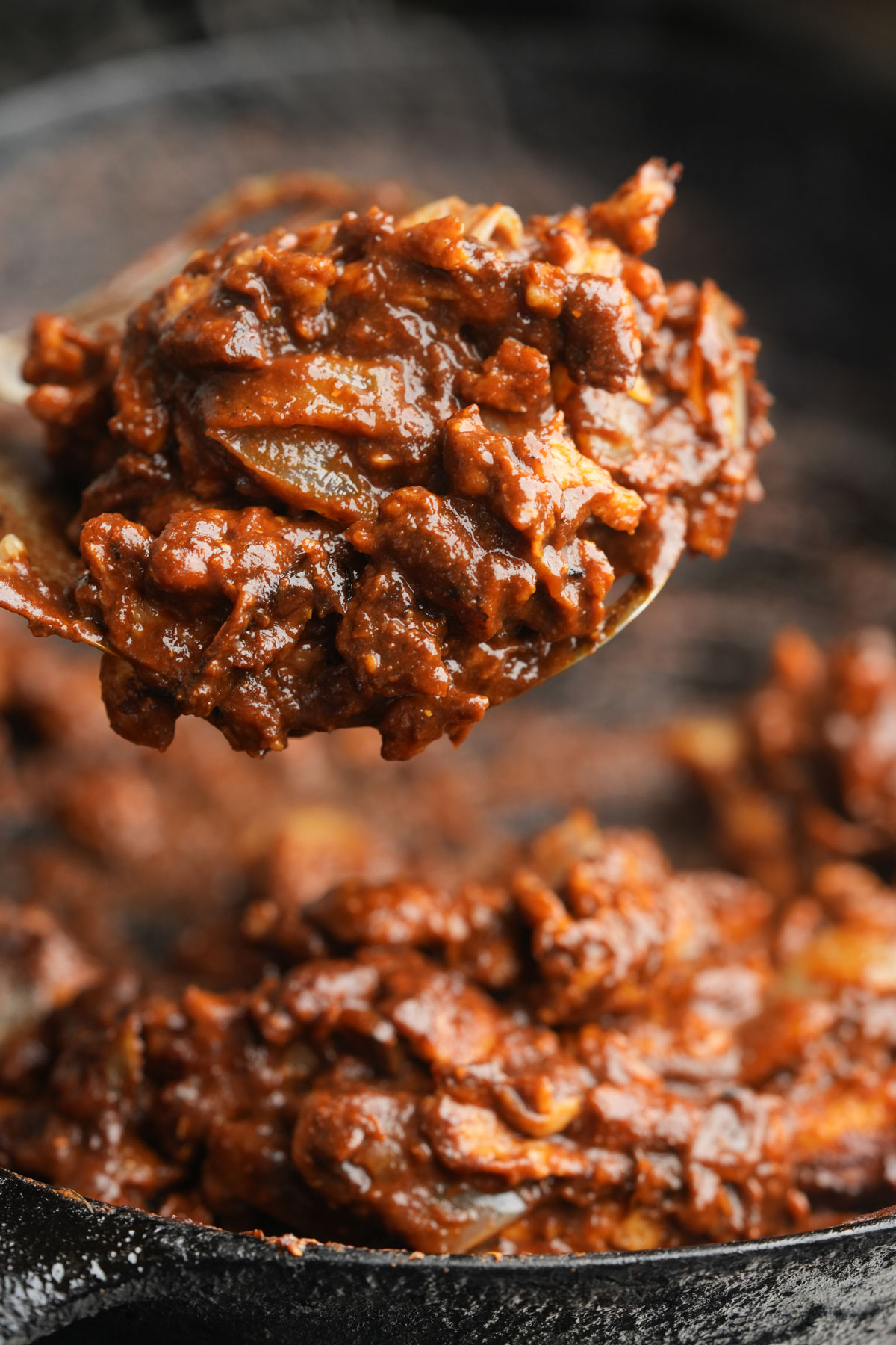 Close-up of a spoon holding cooked vegan chicken mole in a cast iron skillet, with more of the mixture visible in the pan below.