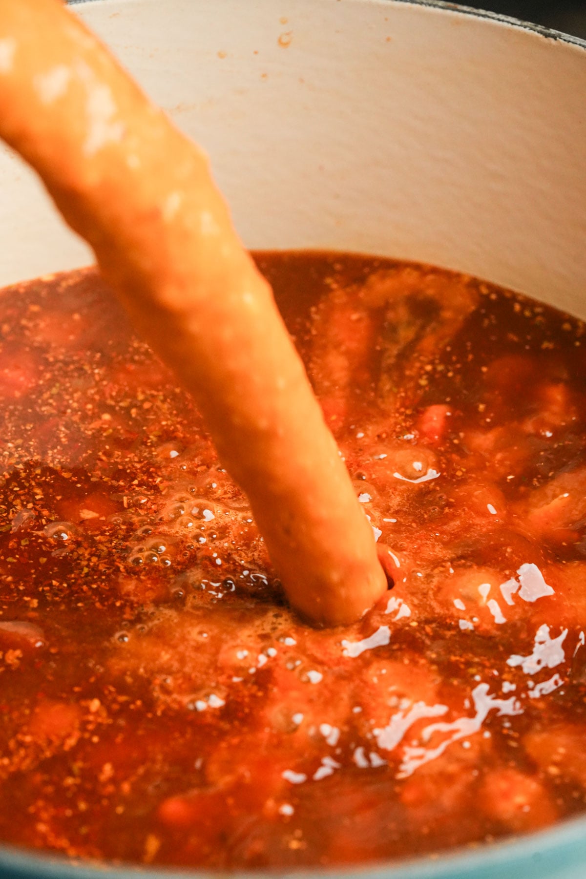A blender is pouring pureed soup back into pot of vegan pozole rojo.
