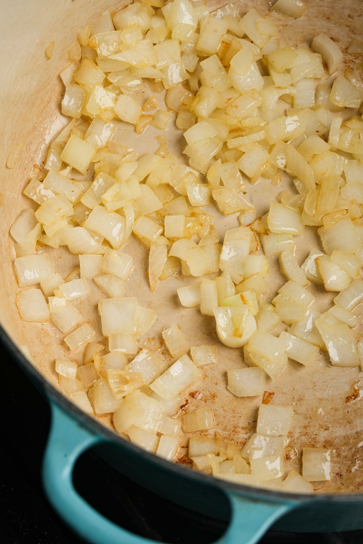 Diced onions sautéing in a light blue pot, turning translucent and golden brown, indicating they are being cooked.
