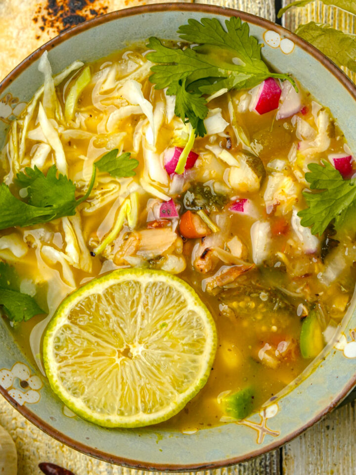 A bowl of vegan pozole verde with a lime wedge and a tortilla.