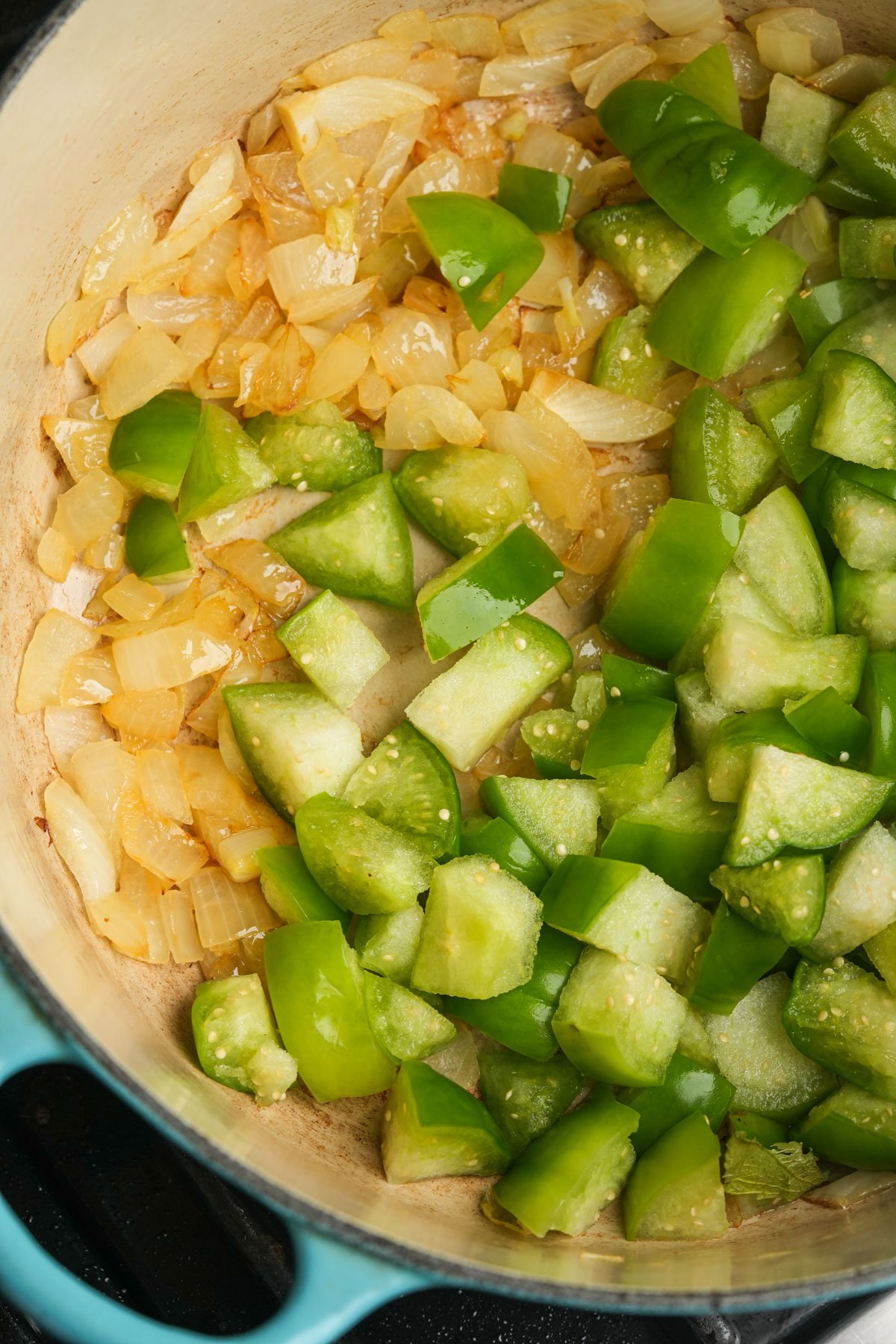 Chopped onions and tomatillos are sautéing in a large, light blue pot.