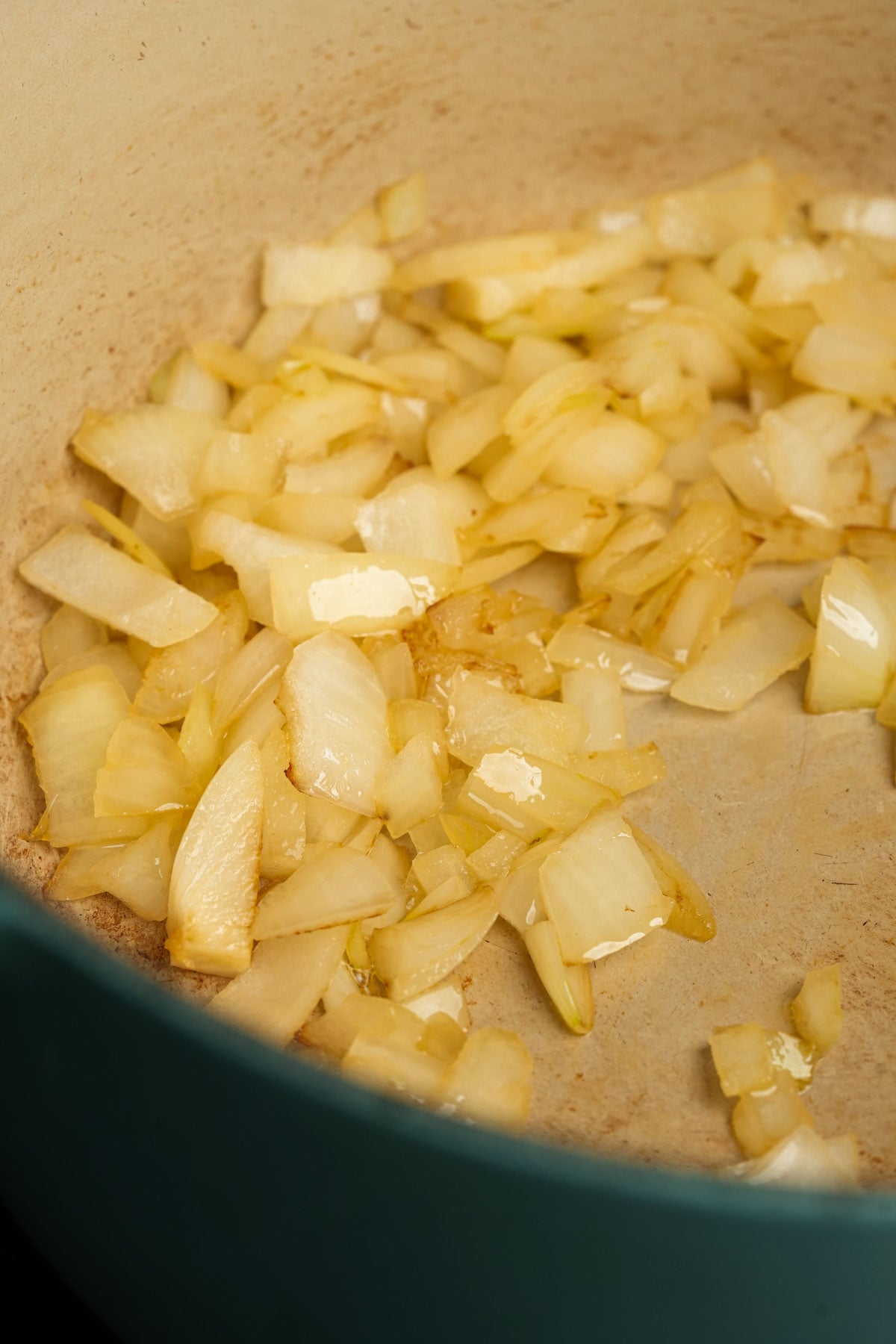 Chopped onions sautéing in oil in a pot, beginning to turn translucent with some light browning visible on the edges.