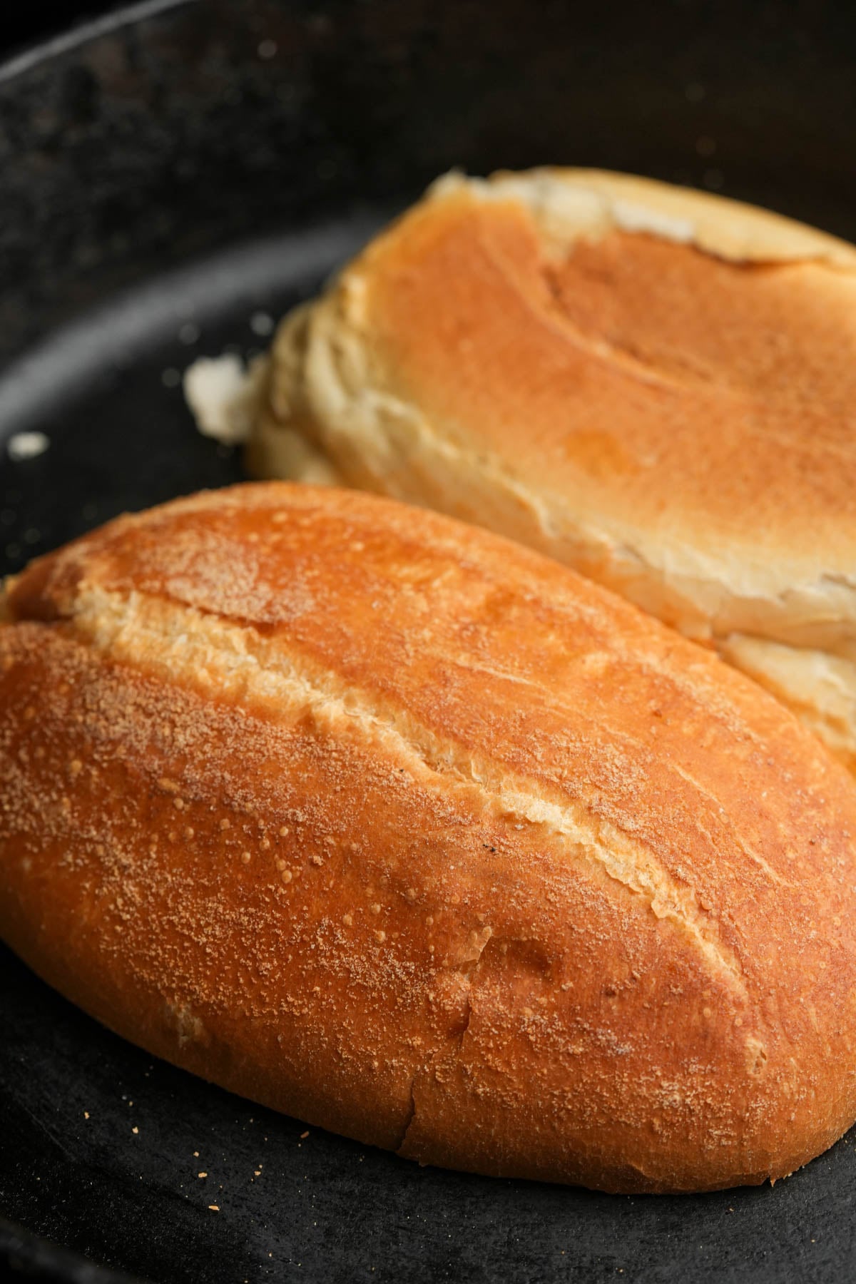 Two pieces of toasted bread, one with a golden brown crust and the other lighter in color, resting on a dark surface.