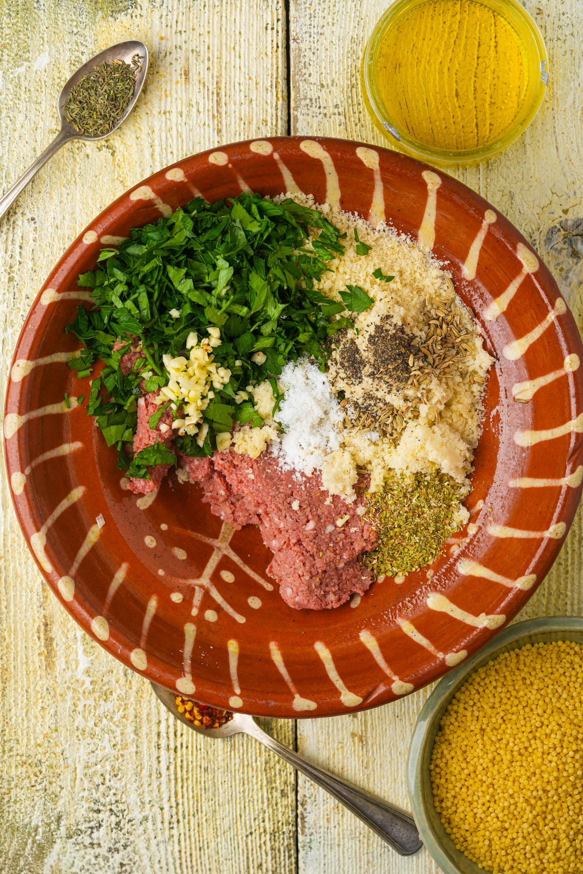A clay bowl holds raw Beyond Meat, chopped parsley, minced garlic, breadcrumbs, spices, and salt.