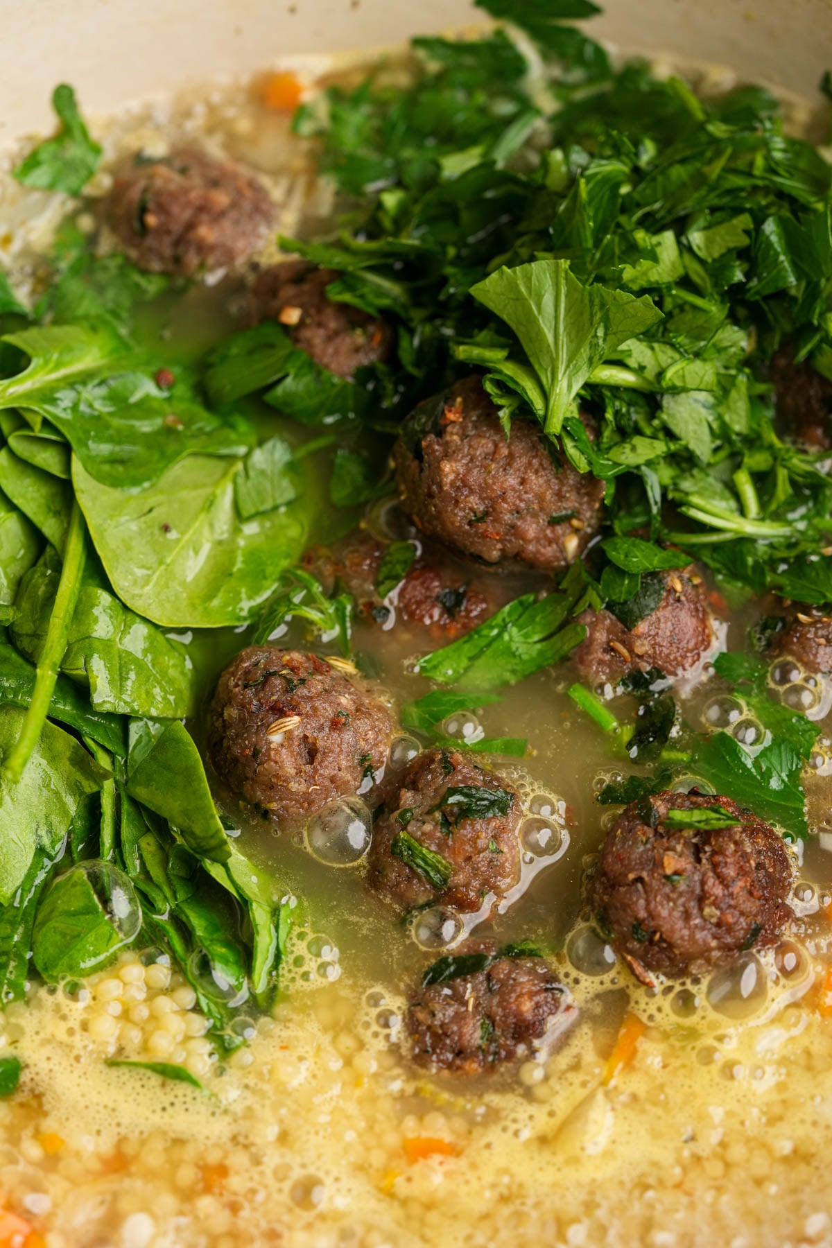 Vegan Italian wedding soup in a pot, showing meatballs, fresh spinach, parsley, acini di pepe pasta, broth, and chopped vegetables.