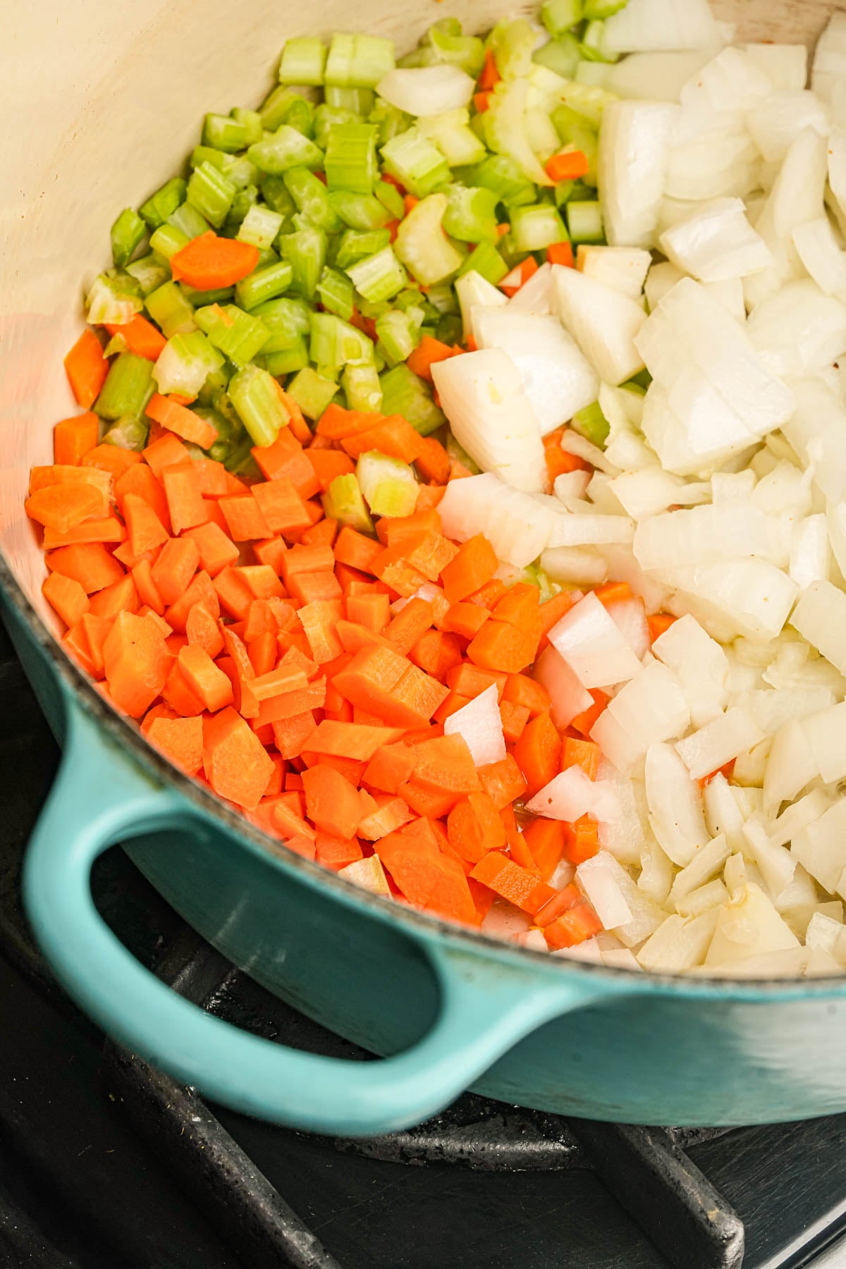 Diced carrots, celery, and onions being sautéed in a green pot on a stove.