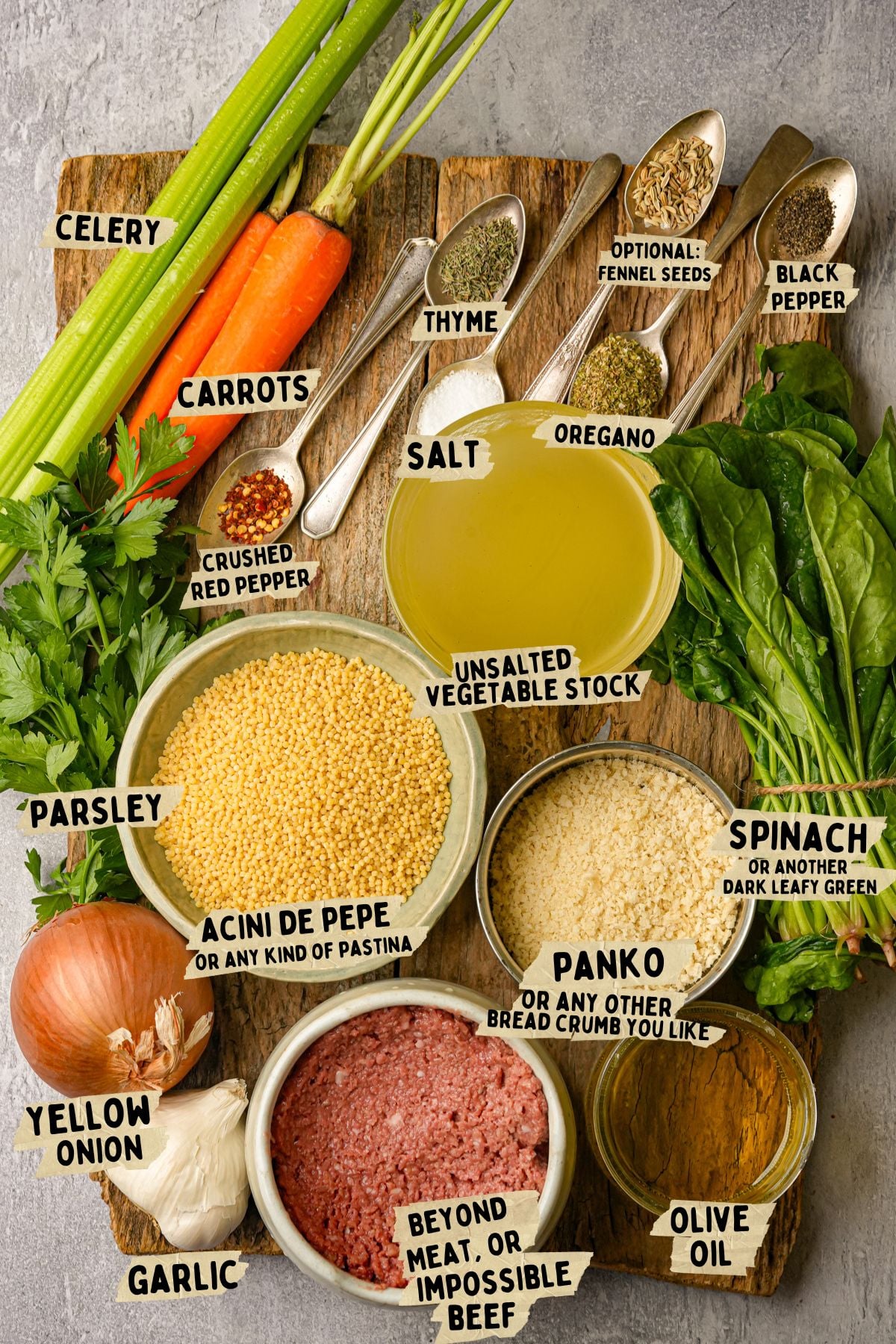 Top-down view of labeled ingredients for a vegan Italian wedding soup recipe, including celery, carrots, fresh herbs, spices, acini di pepe pasta, spinach, panko, yellow onion, garlic, vegetable stock, and plant-based ground beef.