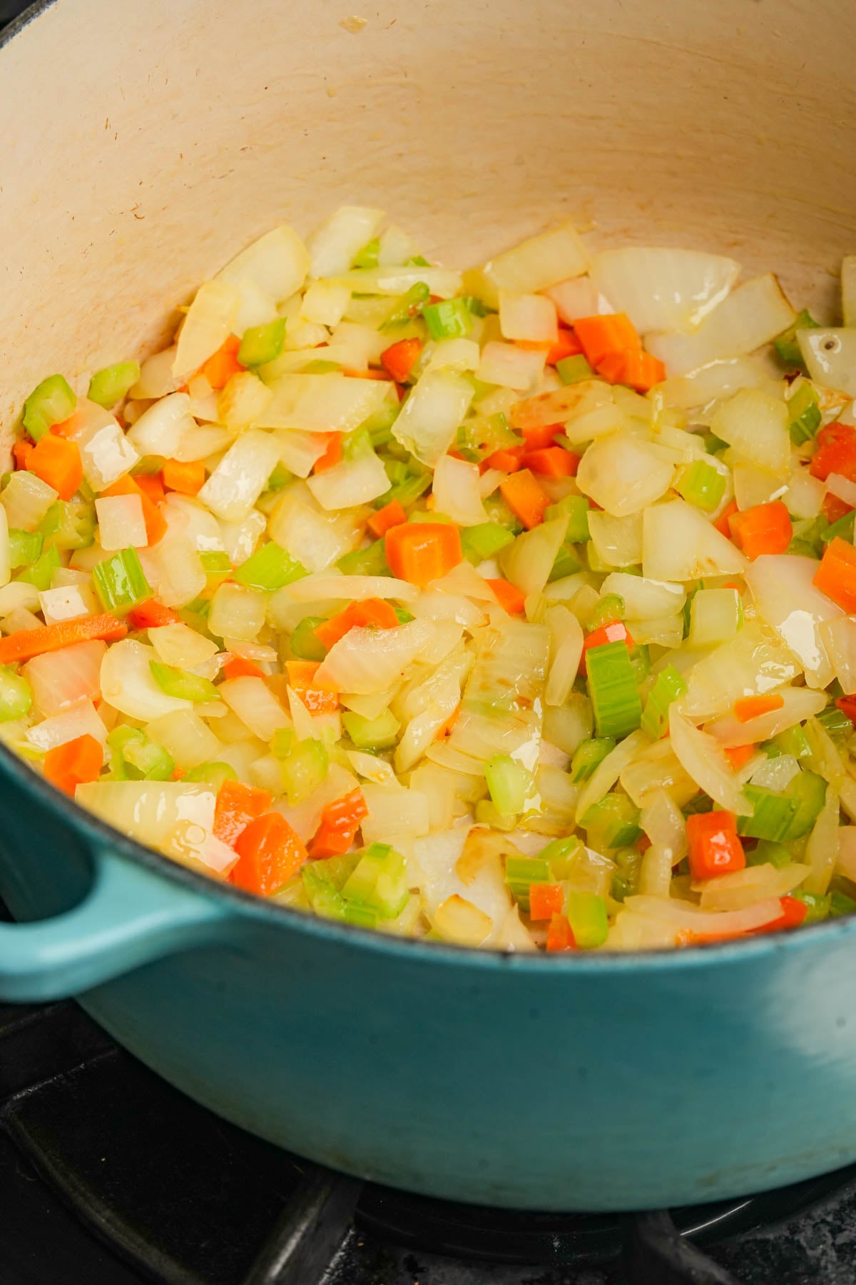 Diced onions, celery, and carrots sautéing in a large blue Dutch oven on a stovetop.