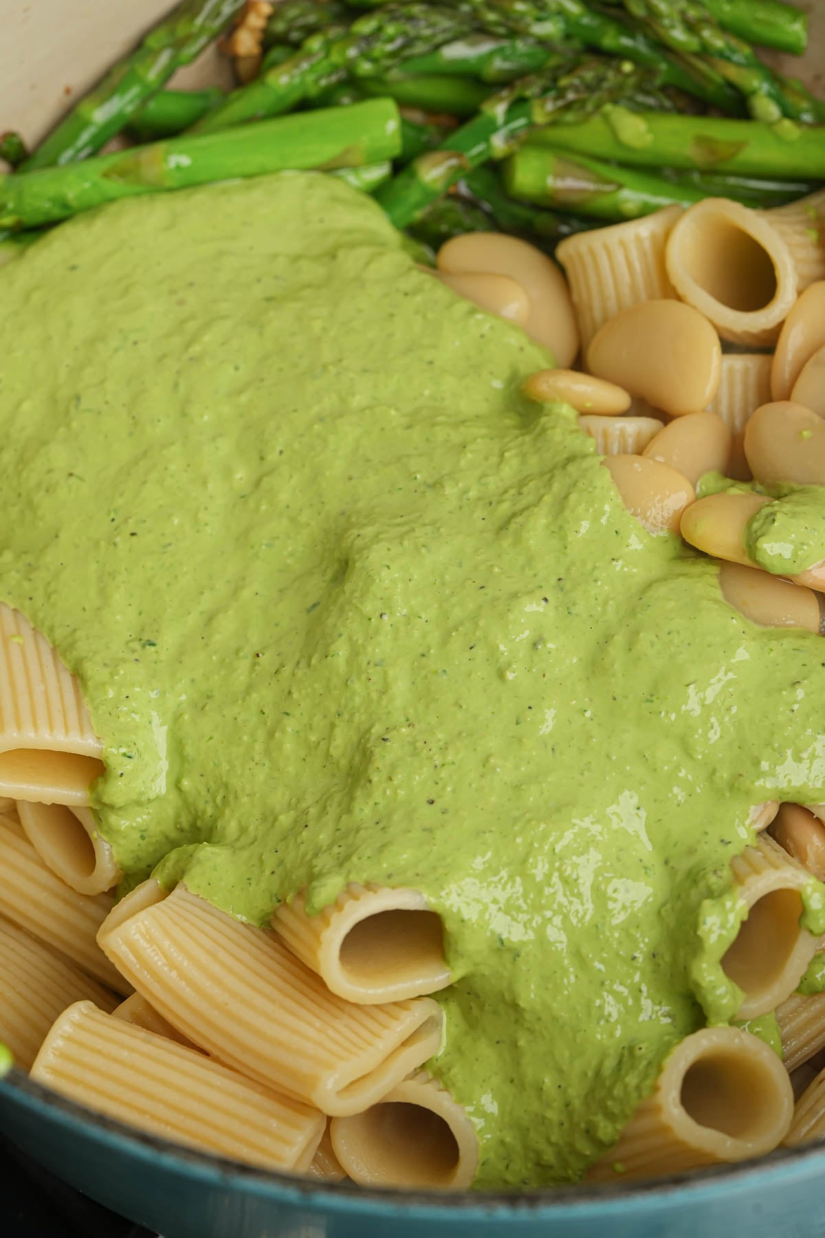 A pan with large rigatoni noodles, cooked asparagus, and a creamy green pesto sauce covering part of the pasta.