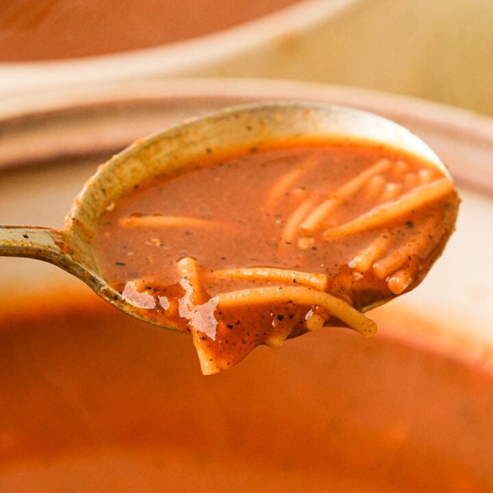 A spoonful pf sopa de fideo above a bowl filled with soup.