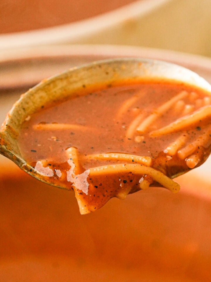 A spoonful pf sopa de fideo above a bowl filled with soup.