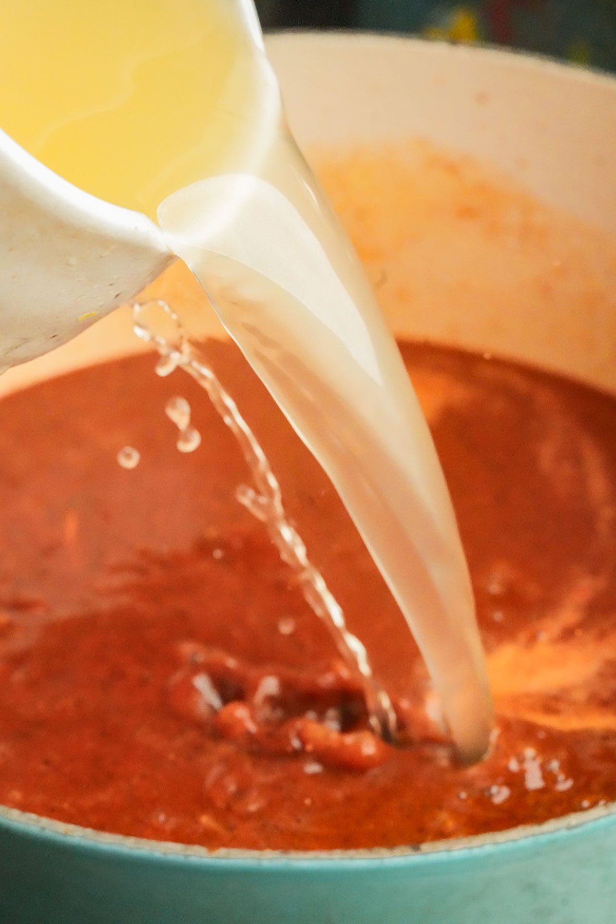 A close-up of broth being poured from a white container into a pot of sopa de fideo.