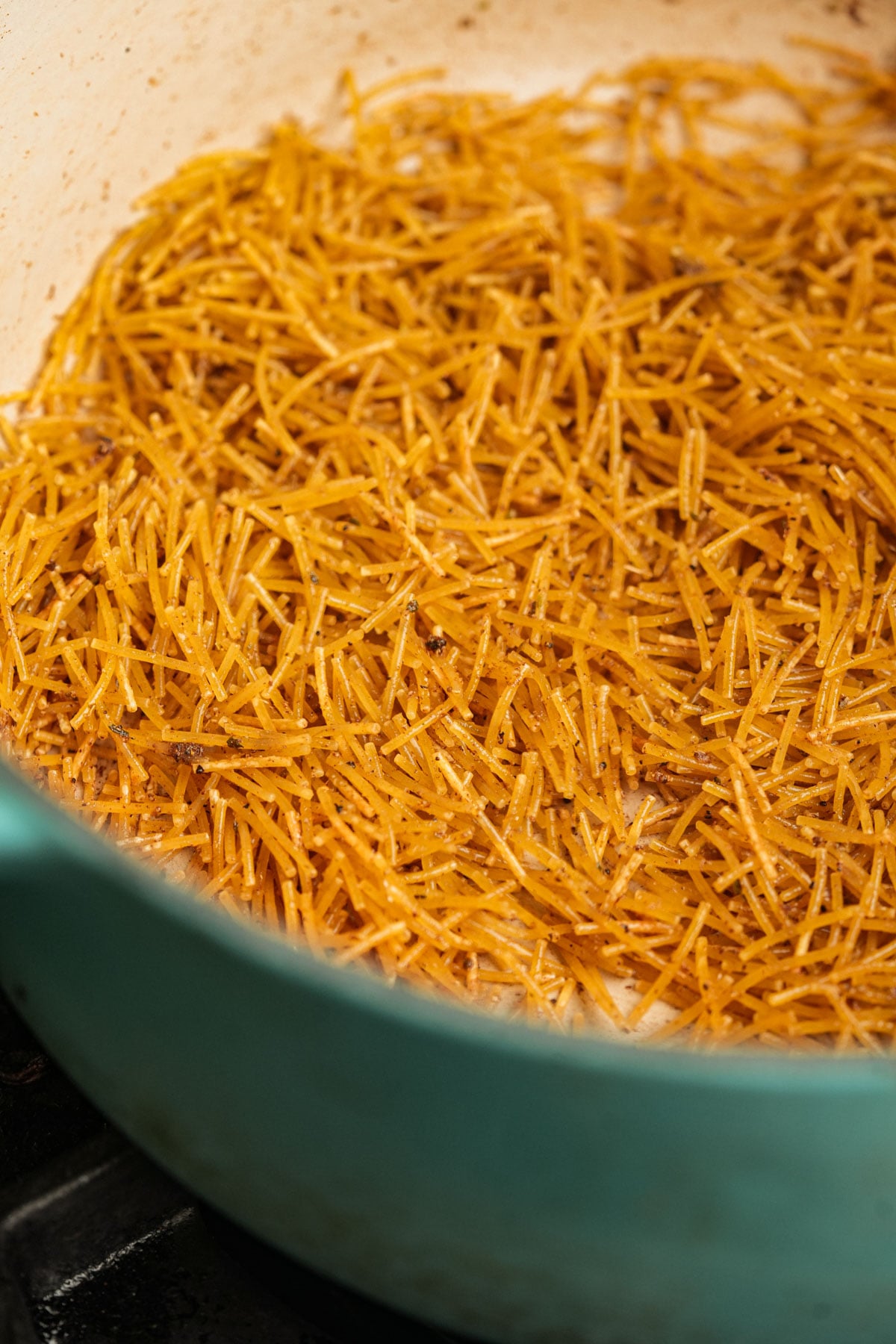 Toasted thin fideo noodles in a blue pot, with the noodles appearing golden brown and slightly crispy.