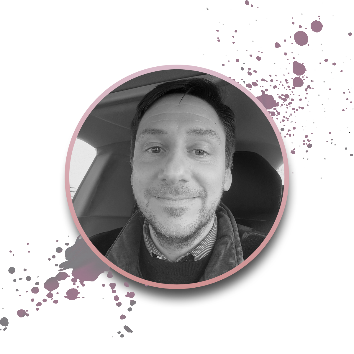 A black and white photo of a smiling man sitting in a car, framed by a pink circular border with paint splatter accents on a white background.