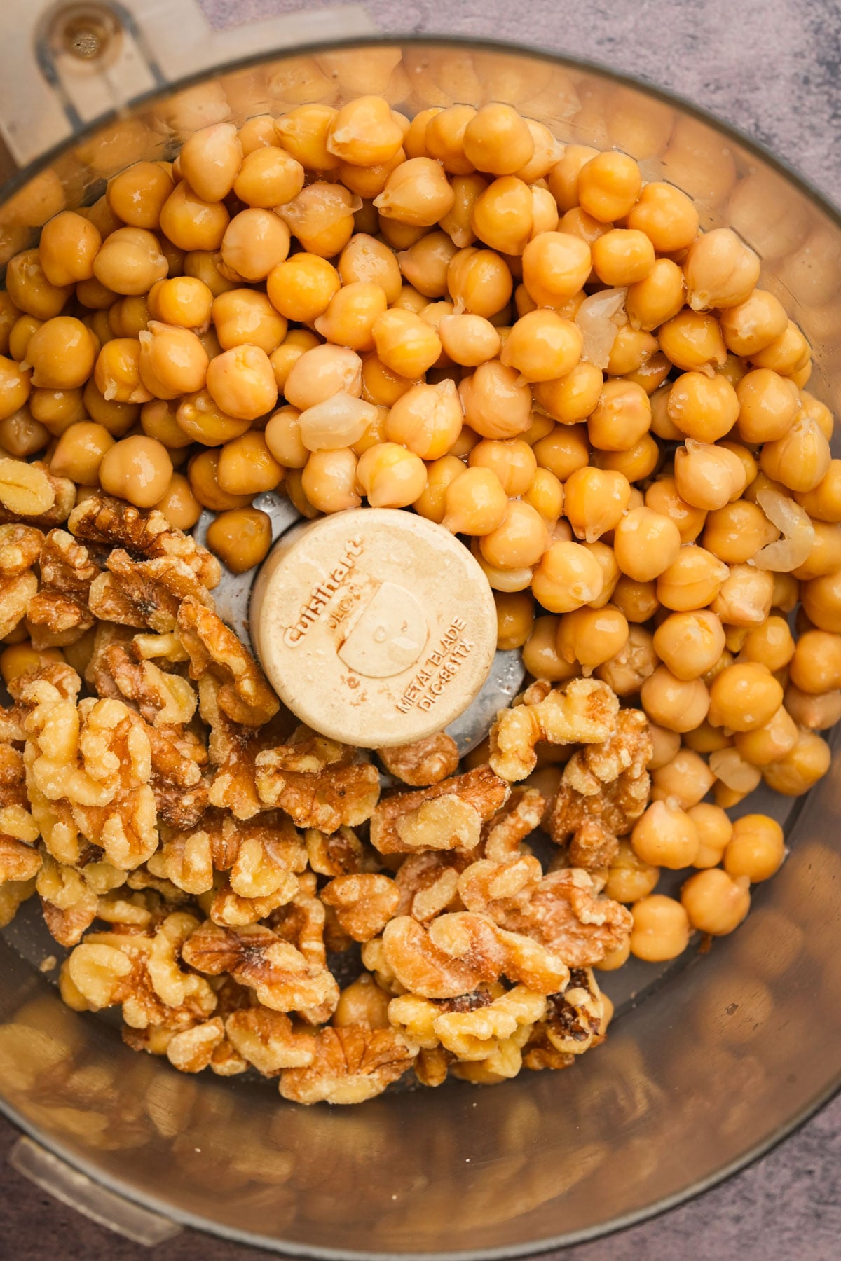 Chickpeas and walnuts in a food processor bowl, ready to be blended, viewed from above.