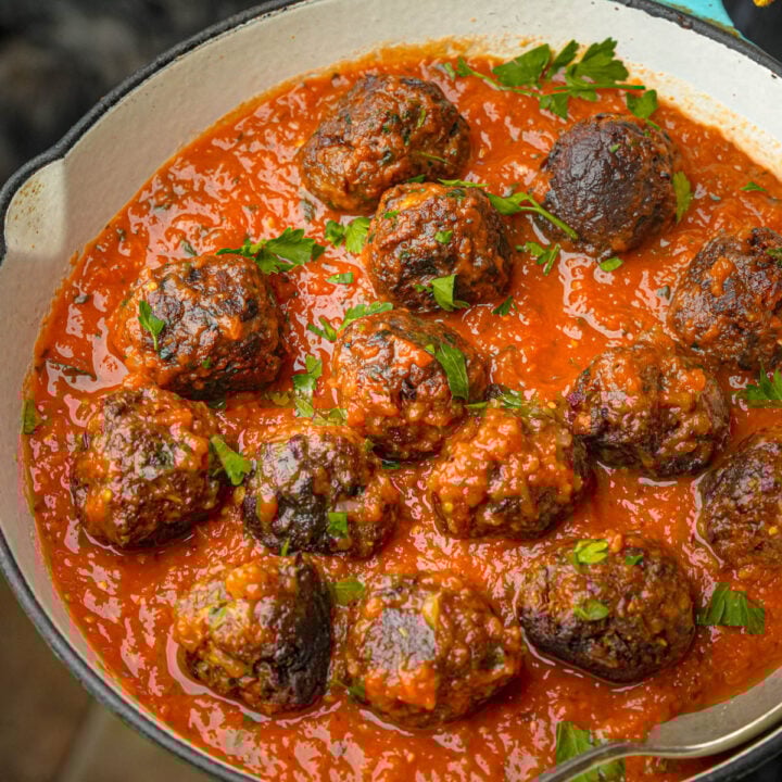 A pan filled with lentil meatballs in a rich tomato sauce, garnished with fresh chopped parsley, with a spoon resting inside the pan.