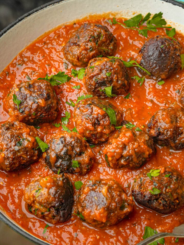 A pan filled with lentil meatballs in a rich tomato sauce, garnished with fresh chopped parsley, with a spoon resting inside the pan.